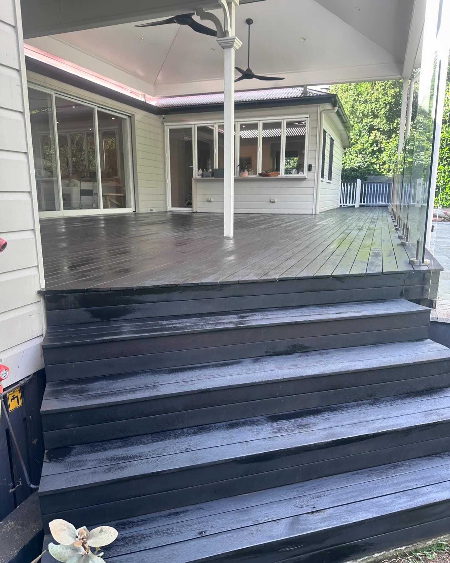Black-stained deck with wide steps leading up to a covered patio