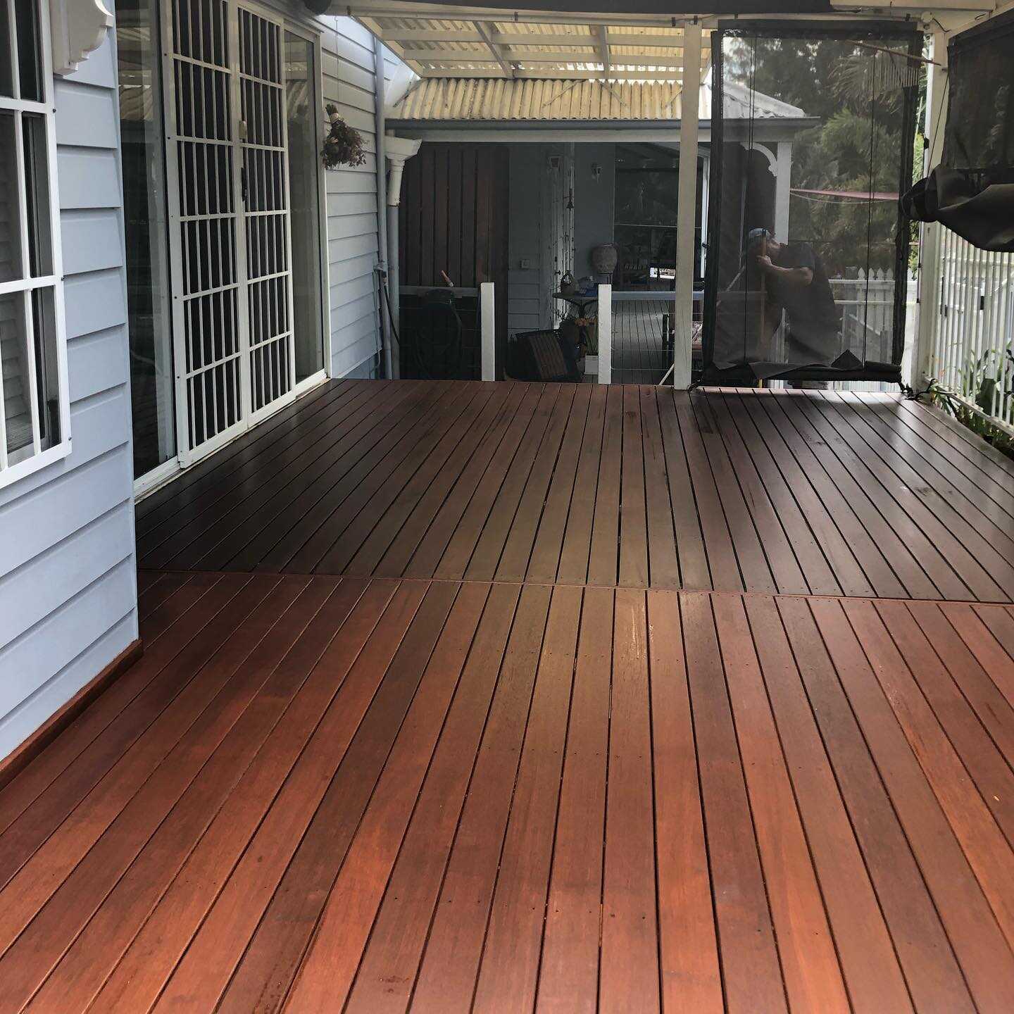 Oiled timber deck under a pergola beside white-framed glass doors