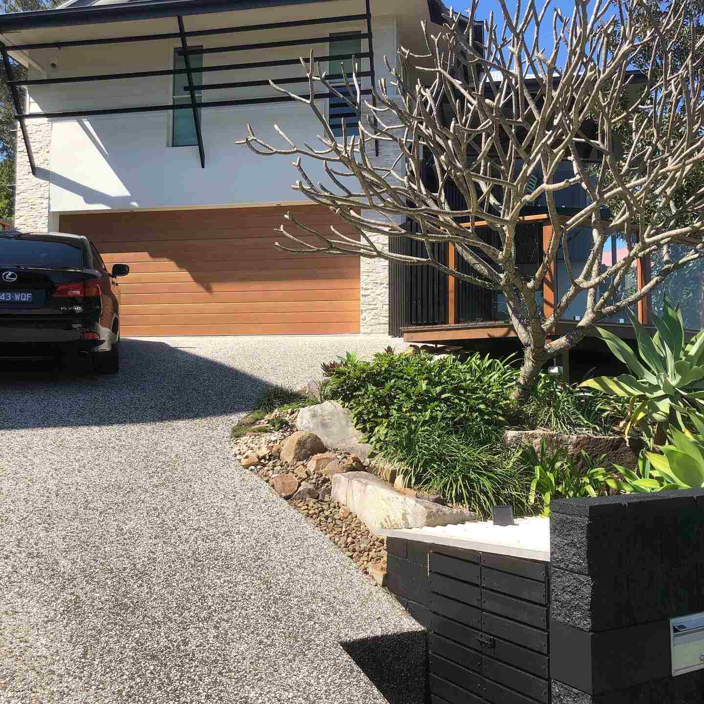 Driveway and garden with a timber garage door and black block letterbox wall