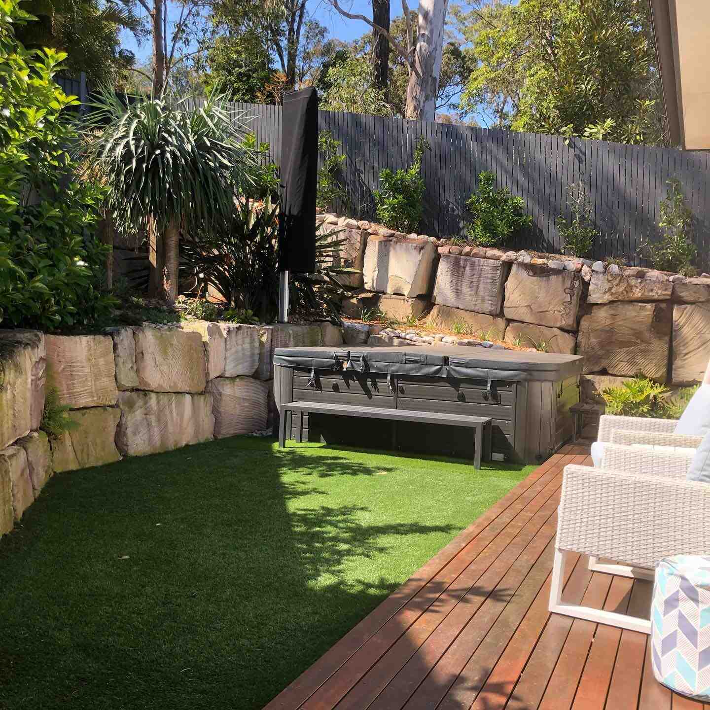 Timber deck beside artificial turf, sandstone retaining walls and a spa