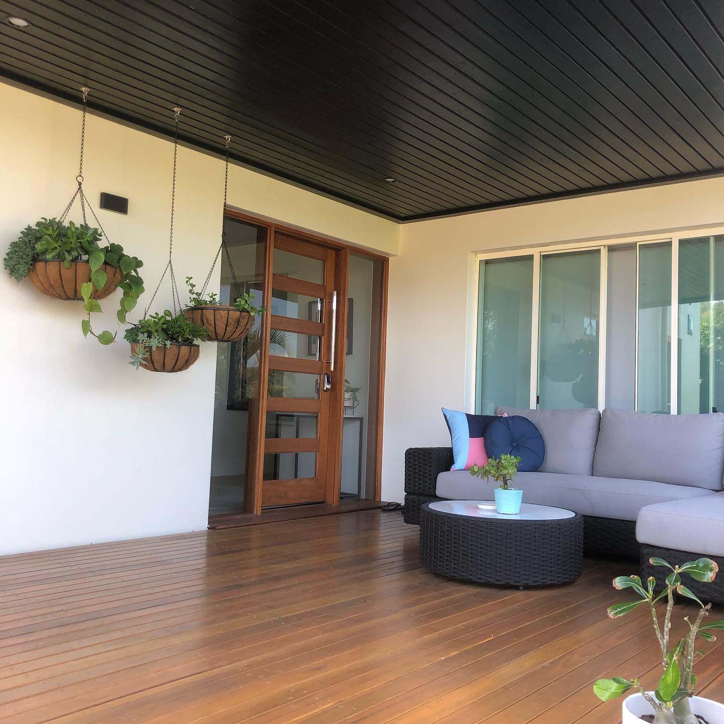Oiled timber deck under a dark ceiling with an outdoor lounge and hanging plants