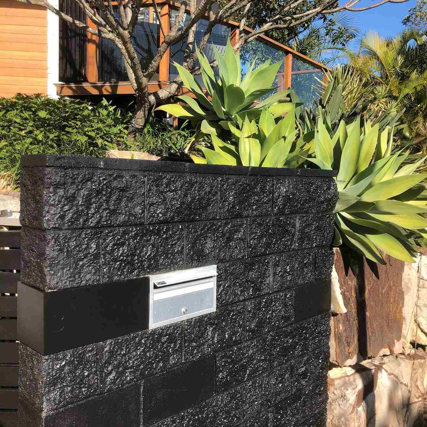 Black block letterbox pillar in front of a garden of agaves