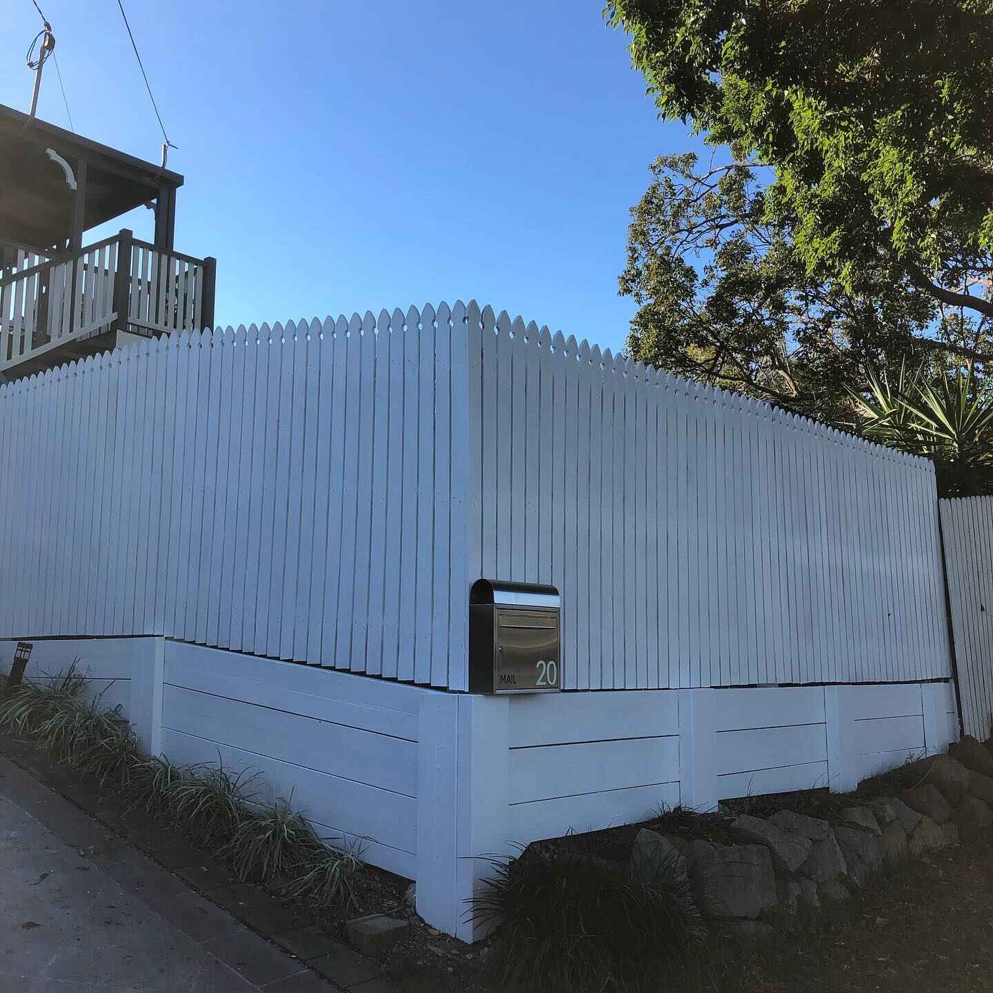 White painted timber fence above a white retaining wall with a letterbox