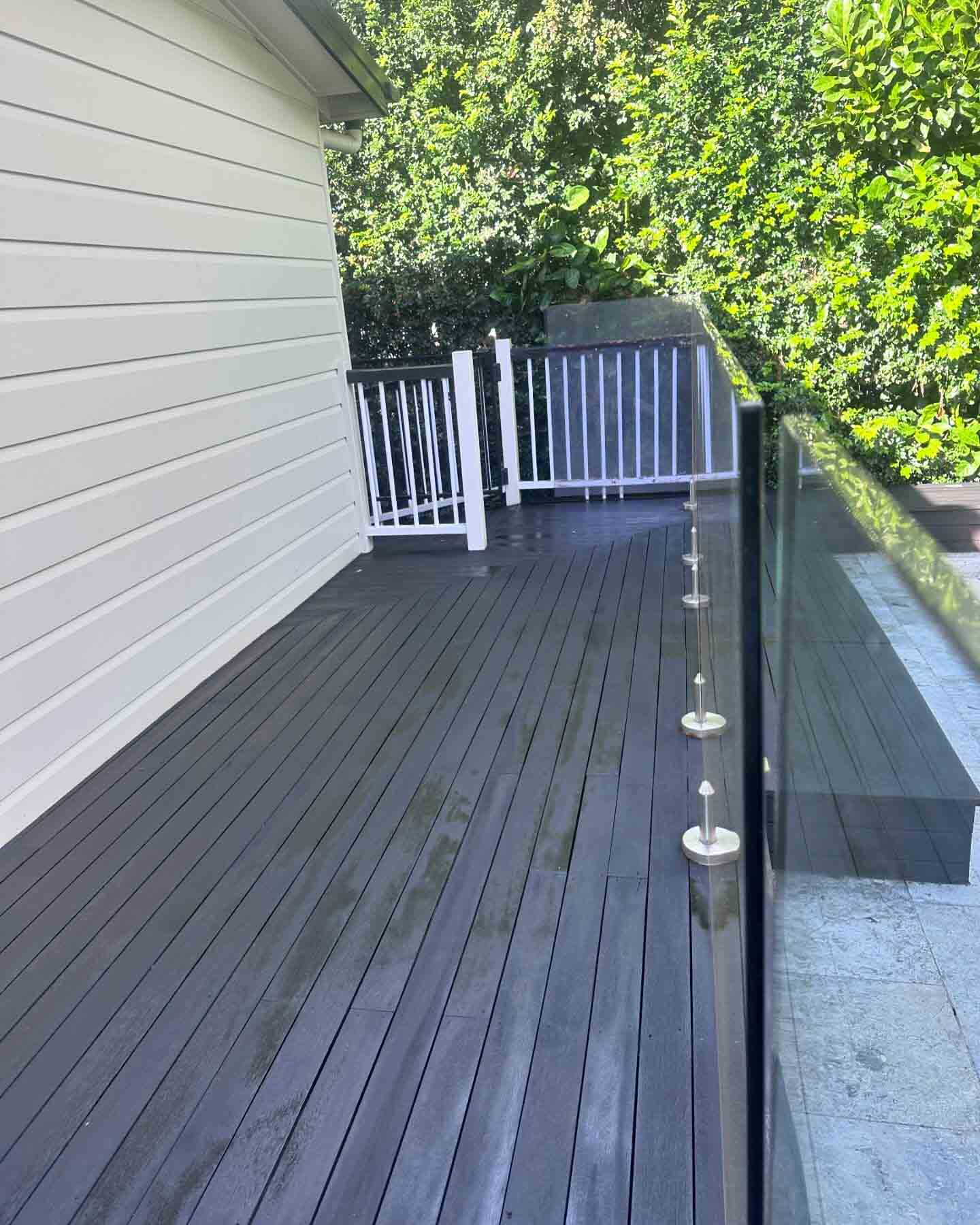 Charcoal-stained deck along a white weatherboard wall with glass balustrade