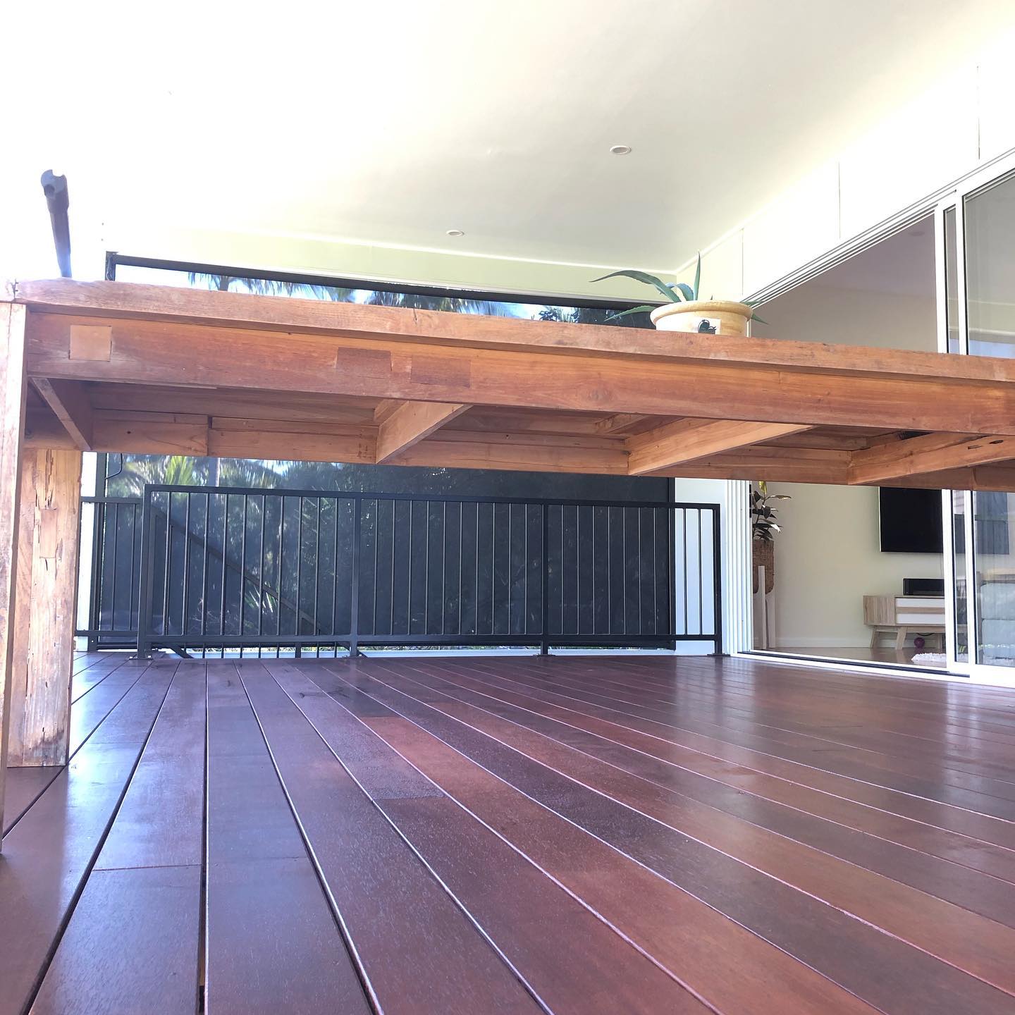 Glossy oiled timber deck beneath a raised timber platform with black balustrade
