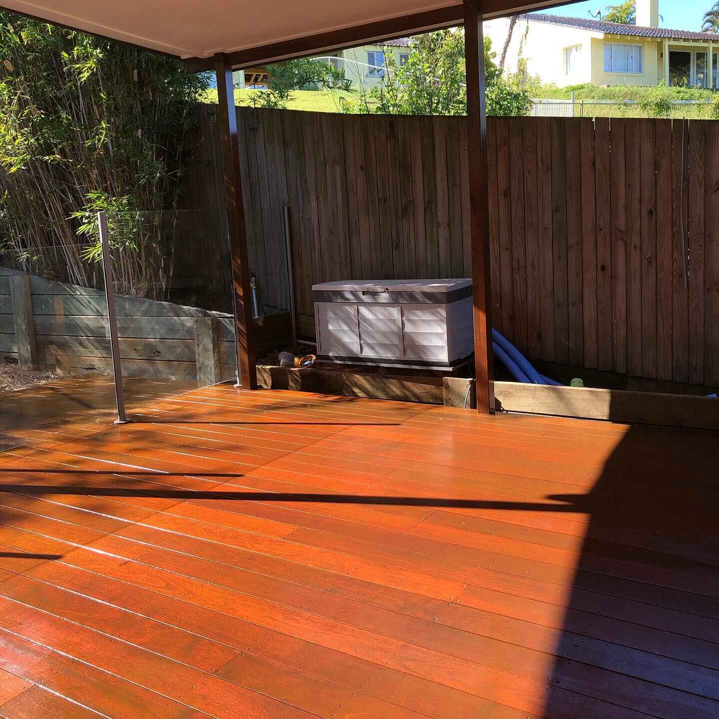 Sunlit oiled timber deck under a patio beside a timber fence