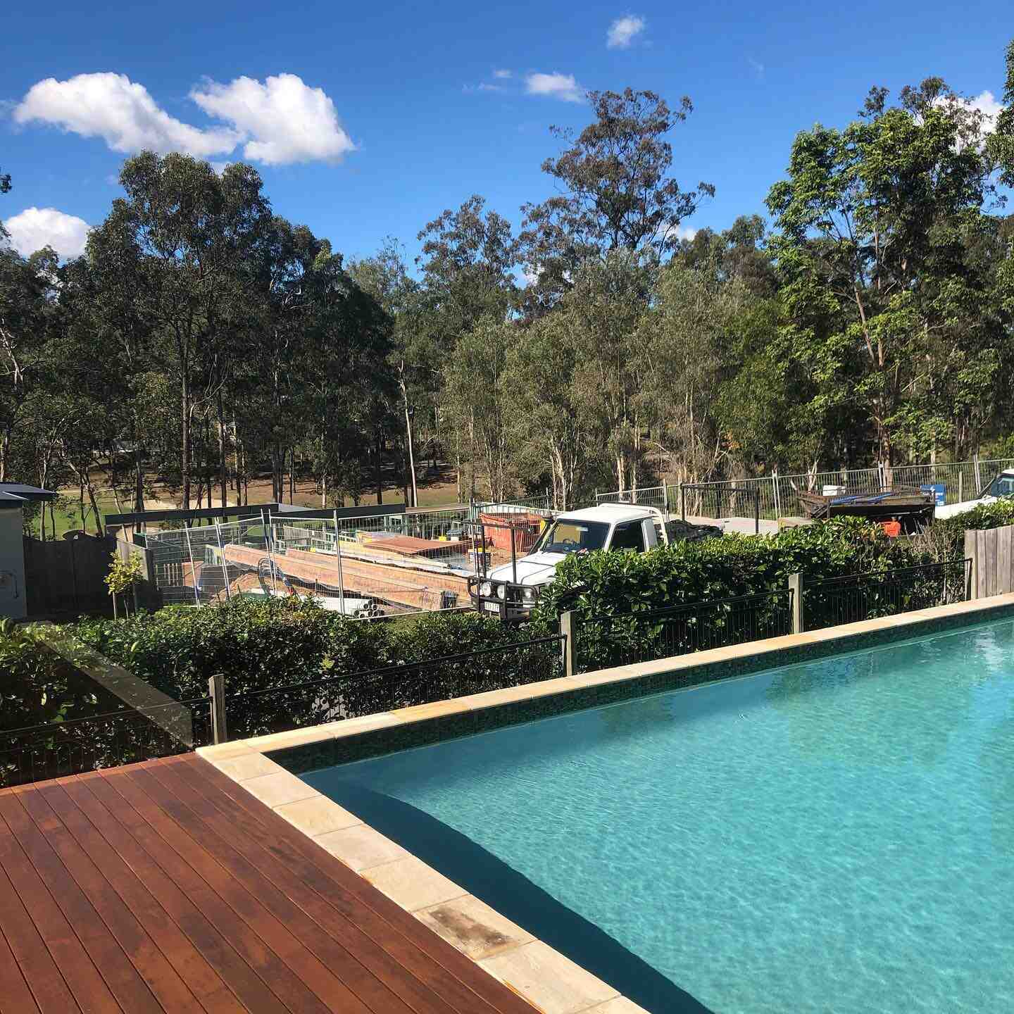 Timber deck beside a pool with a hedge and trees behind