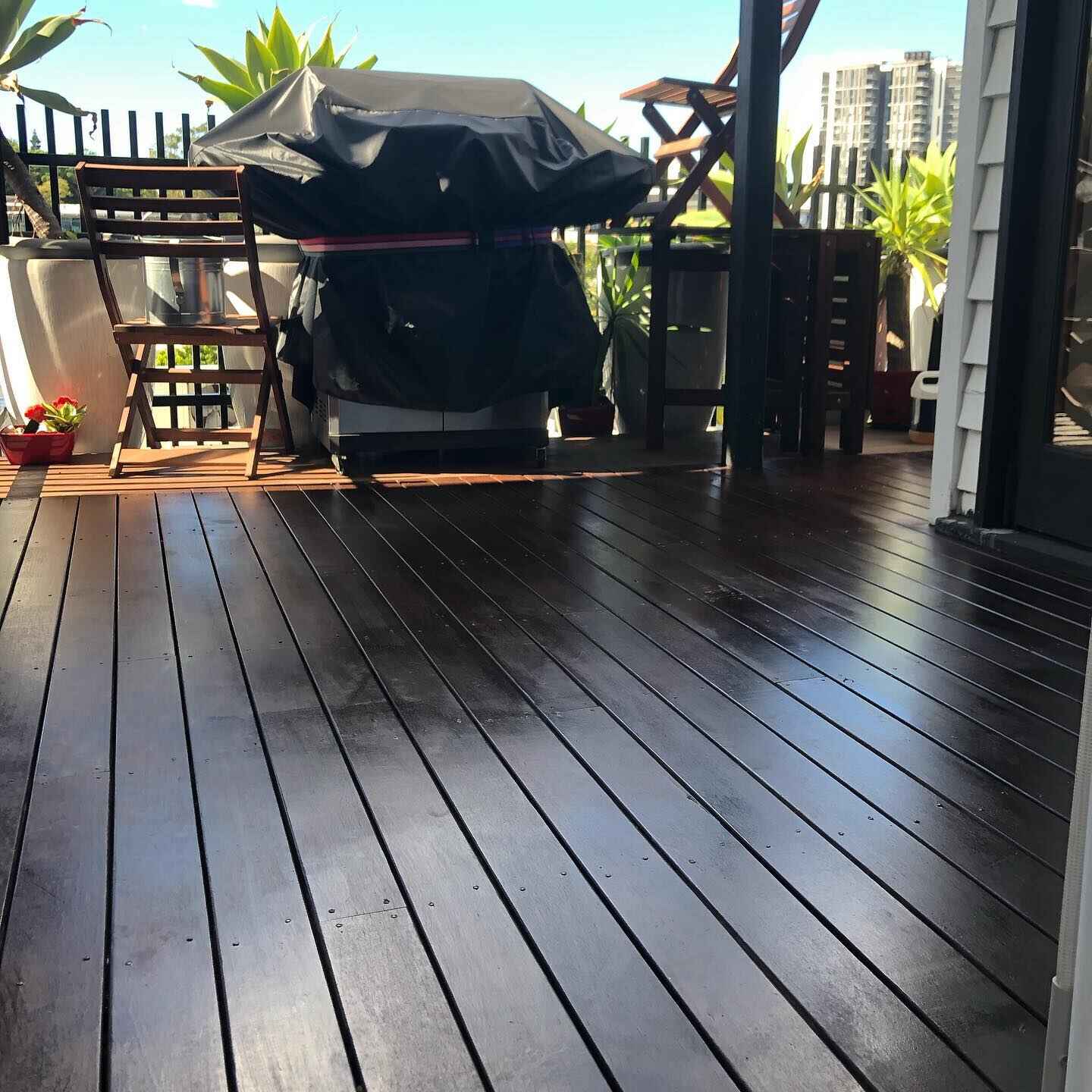 Dark oiled timber deck with a covered barbecue and outdoor chairs