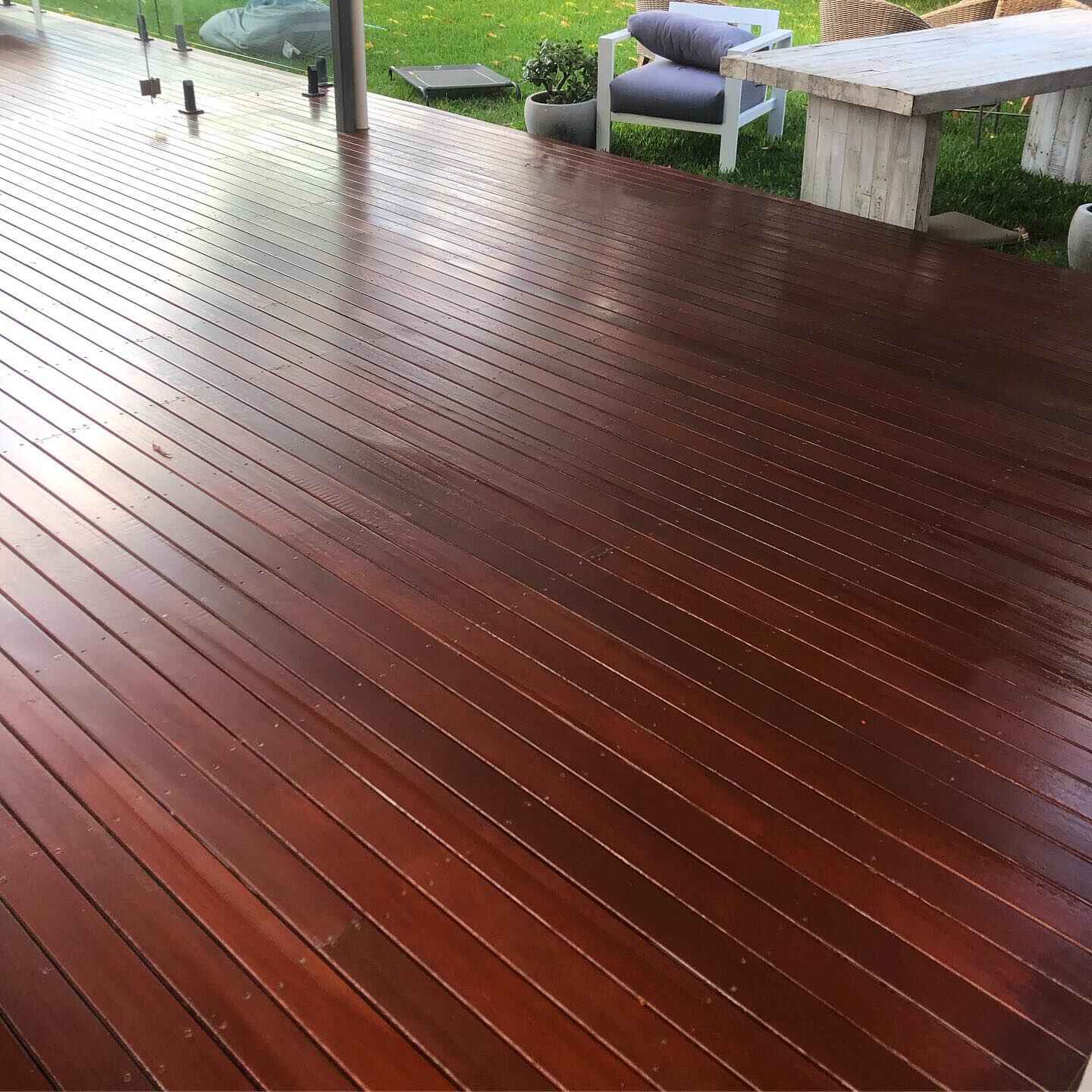 Glossy dark red oiled timber deck beside a lawn with outdoor furniture