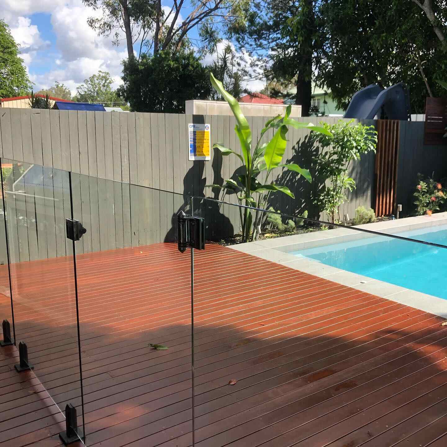 Oiled timber deck around a pool with glass pool fencing