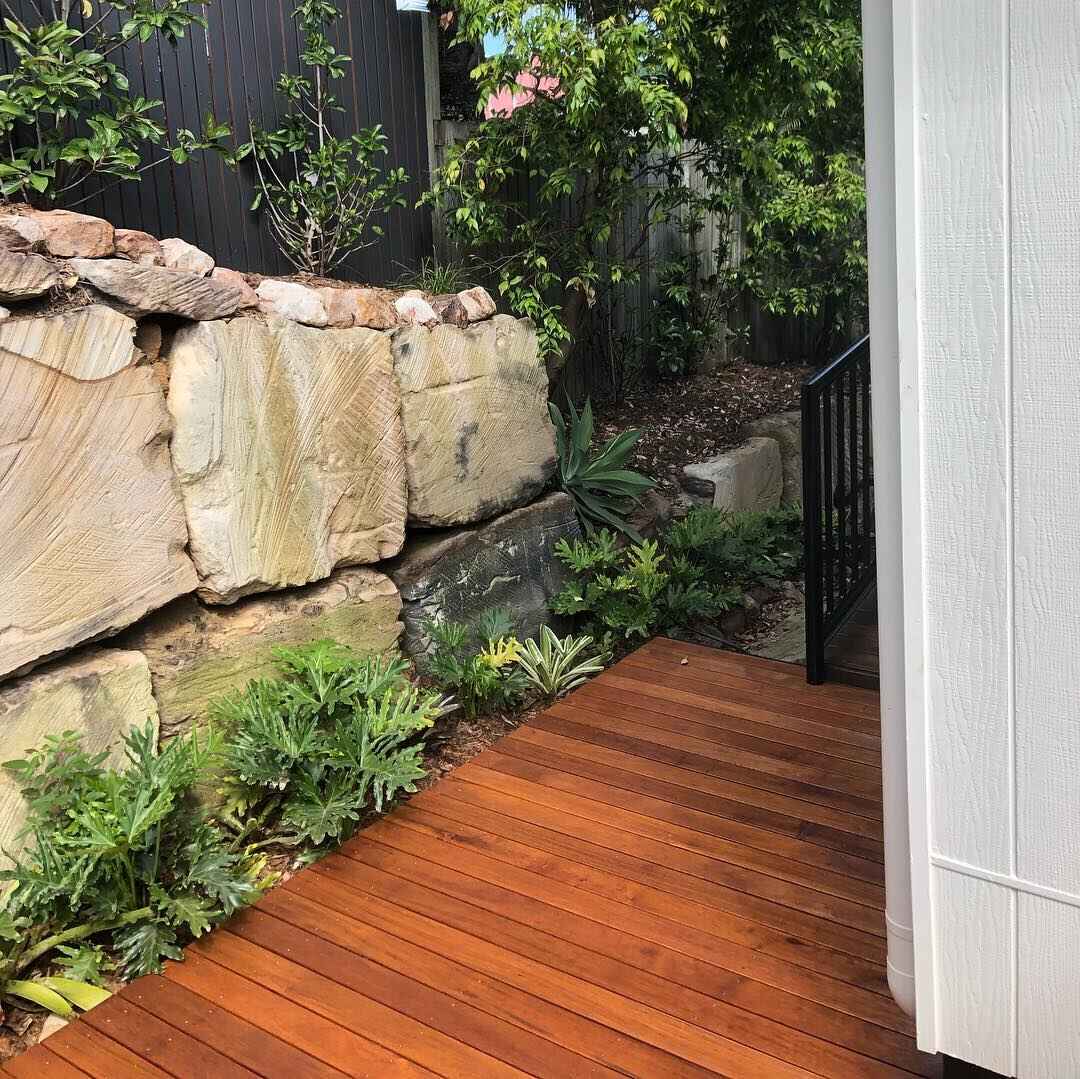 Oiled timber side deck beside a sandstone retaining wall and ferns