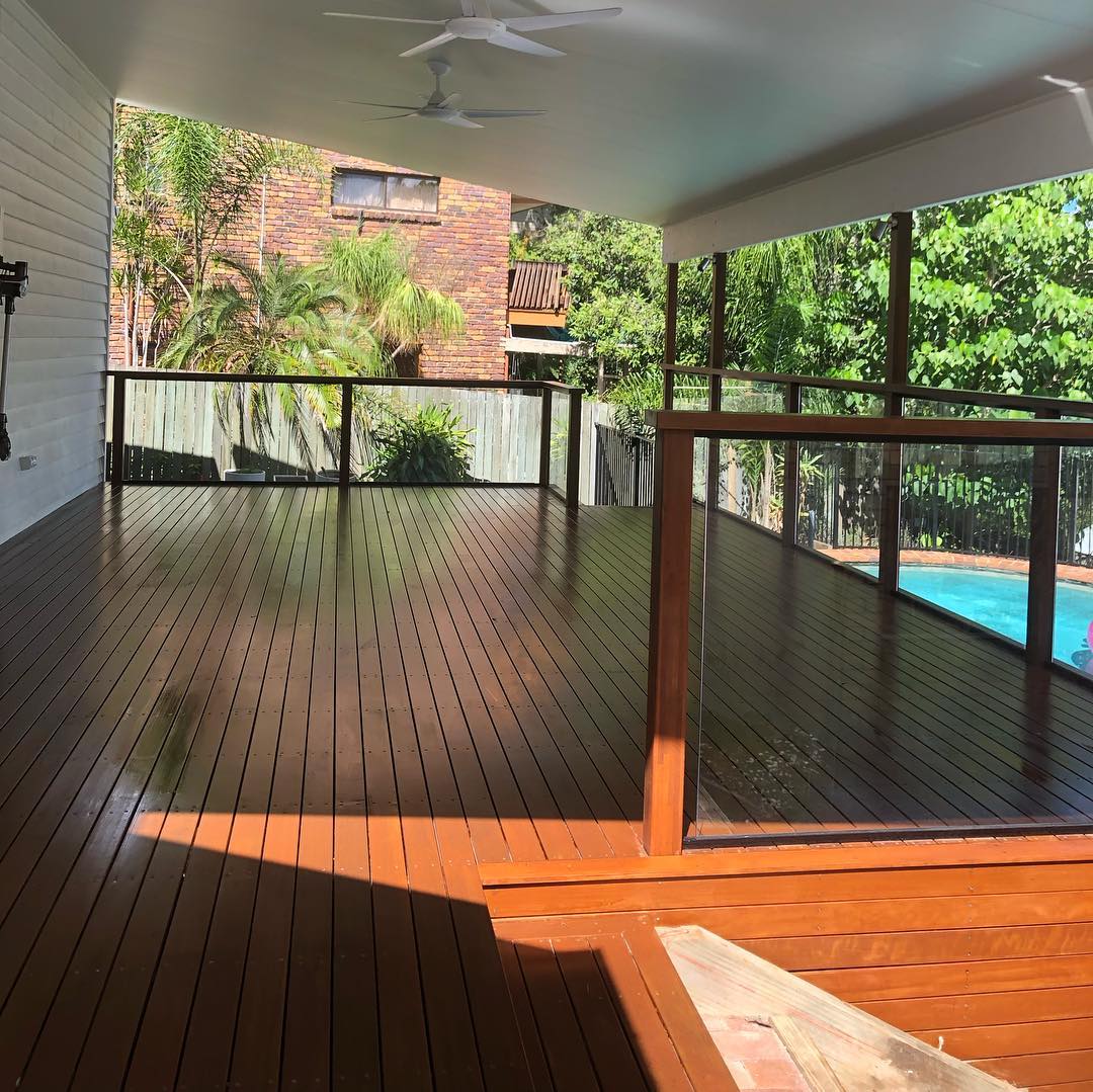 Oiled timber deck under a white roof with timber and glass balustrade above a pool