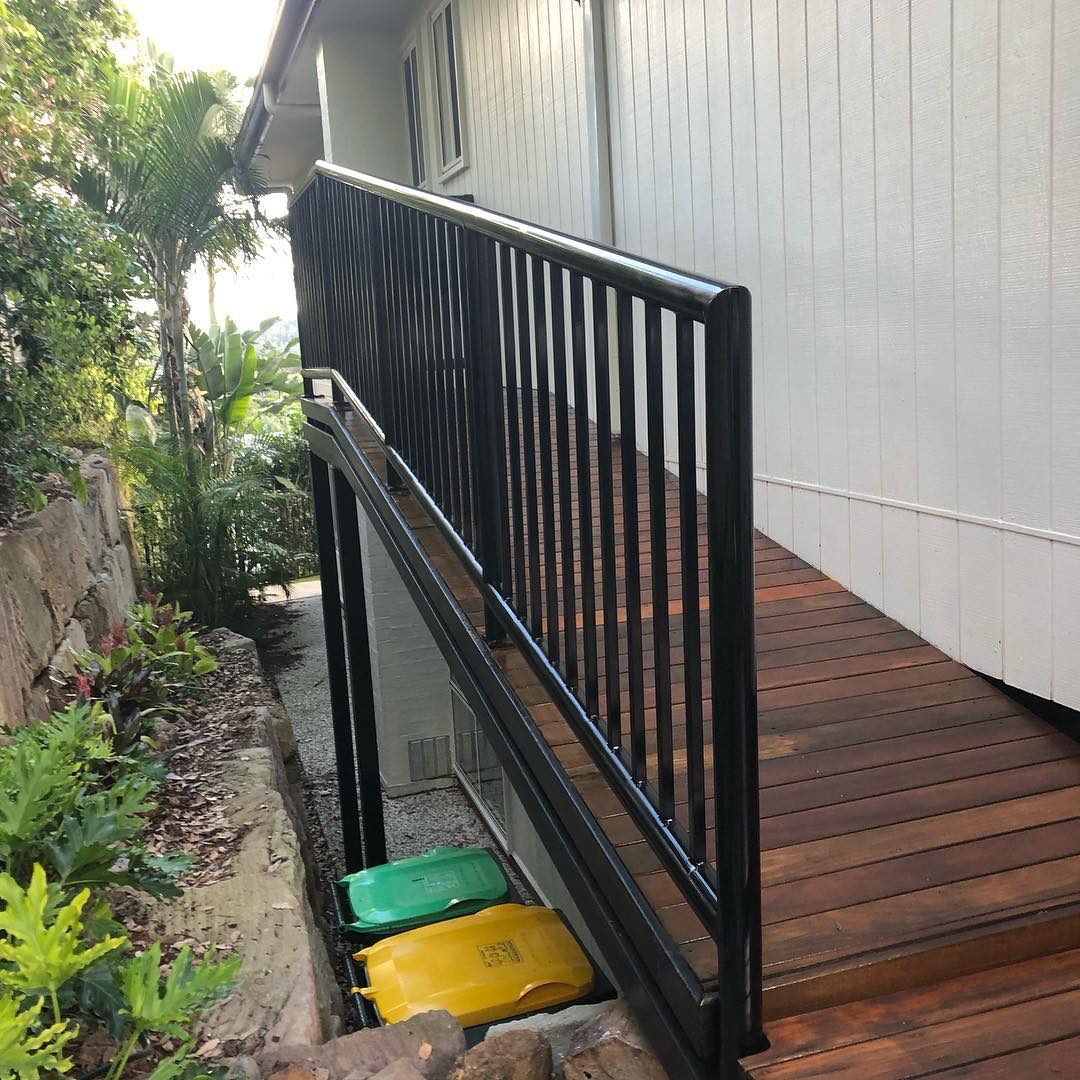 Oiled timber side deck with black balustrade beside a white house