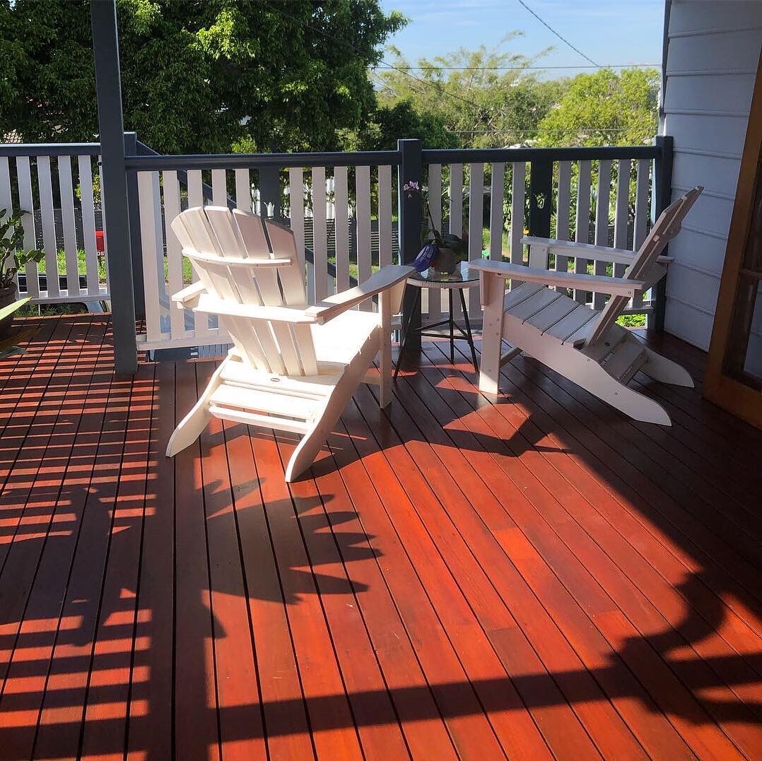 Red-toned oiled timber deck with two white Adirondack chairs