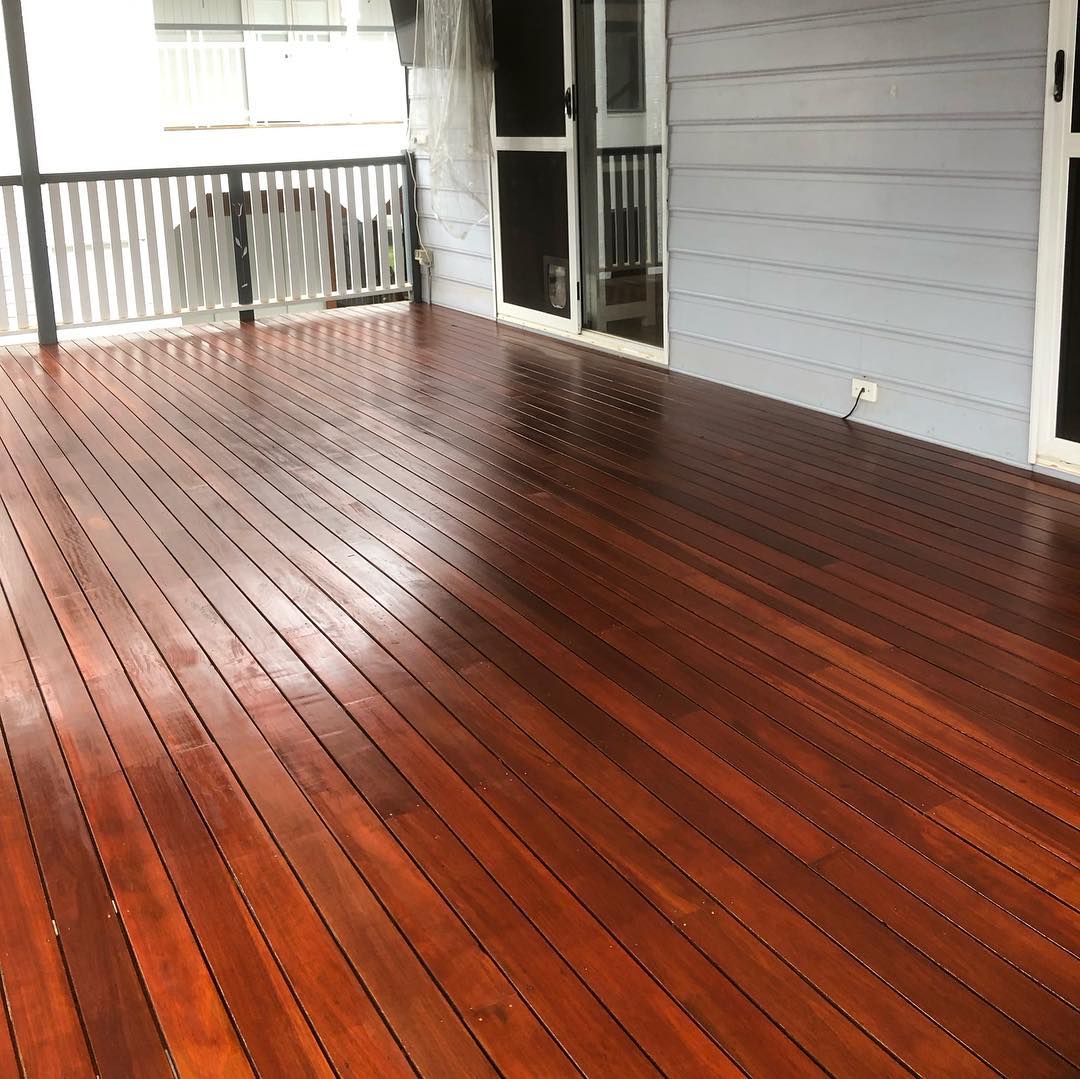 Glossy oiled timber deck beside a grey weatherboard house with black balustrade