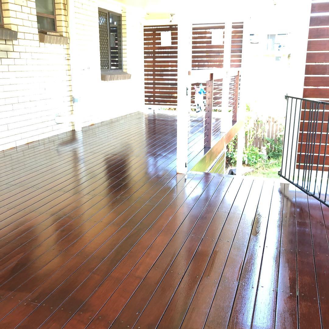 Glossy wet oiled timber deck beside a brick house and timber slat screen