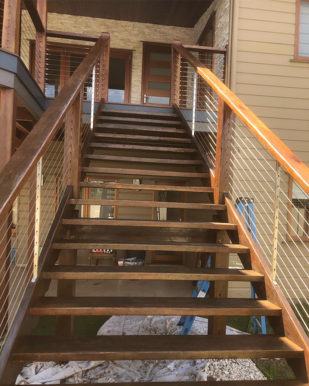 Oiled timber stairs with timber and wire balustrade leading up to a house