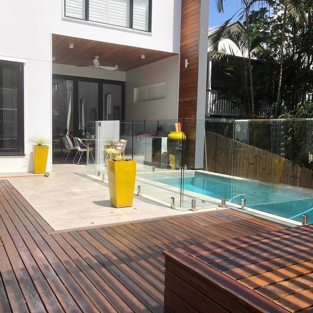 Oiled timber deck with a built-in bench beside a glass-fenced pool