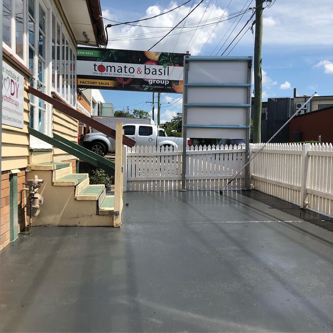 Grey-painted concrete forecourt beside a white picket fence and timber building