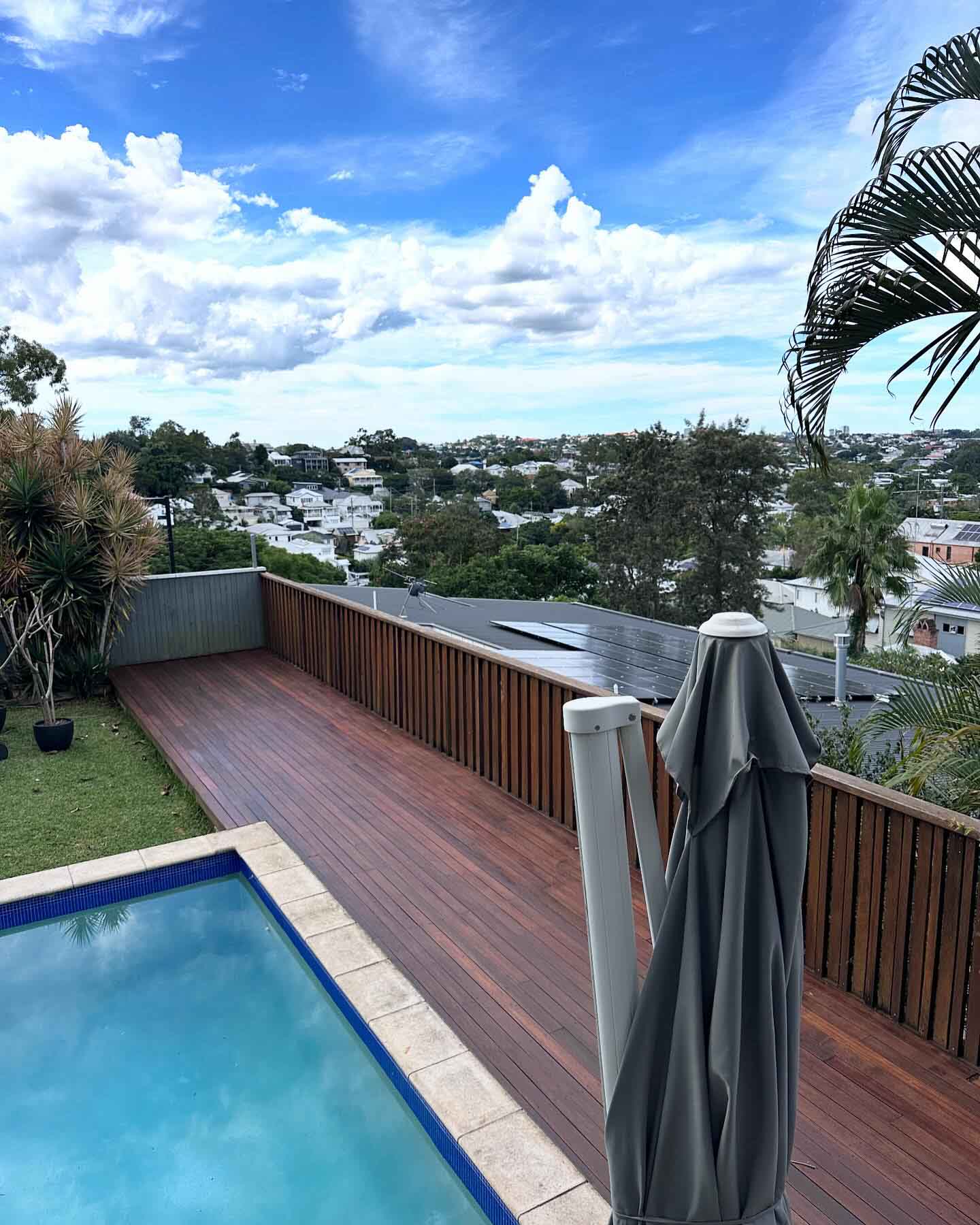 Narrow timber deck with a timber slat screen beside a pool, overlooking the suburbs