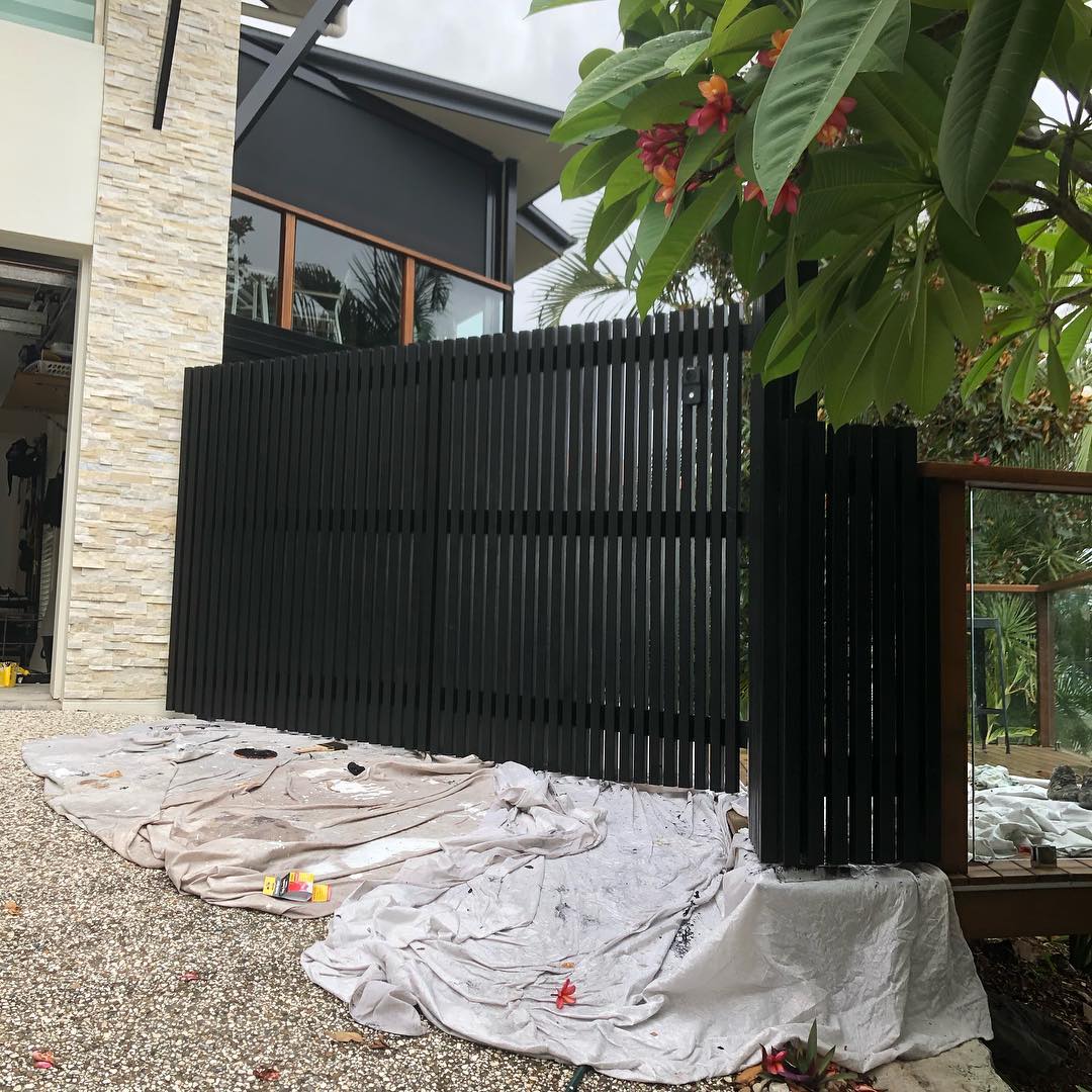 Black vertical batten fence with drop sheets on the gravel below