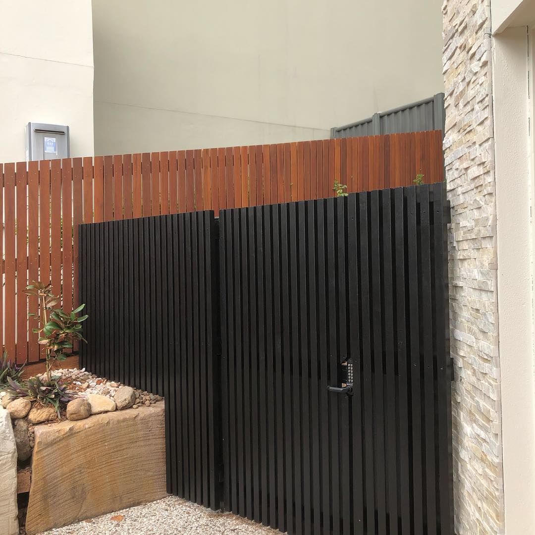 Black batten gate and oiled timber fence beside a stone-clad wall