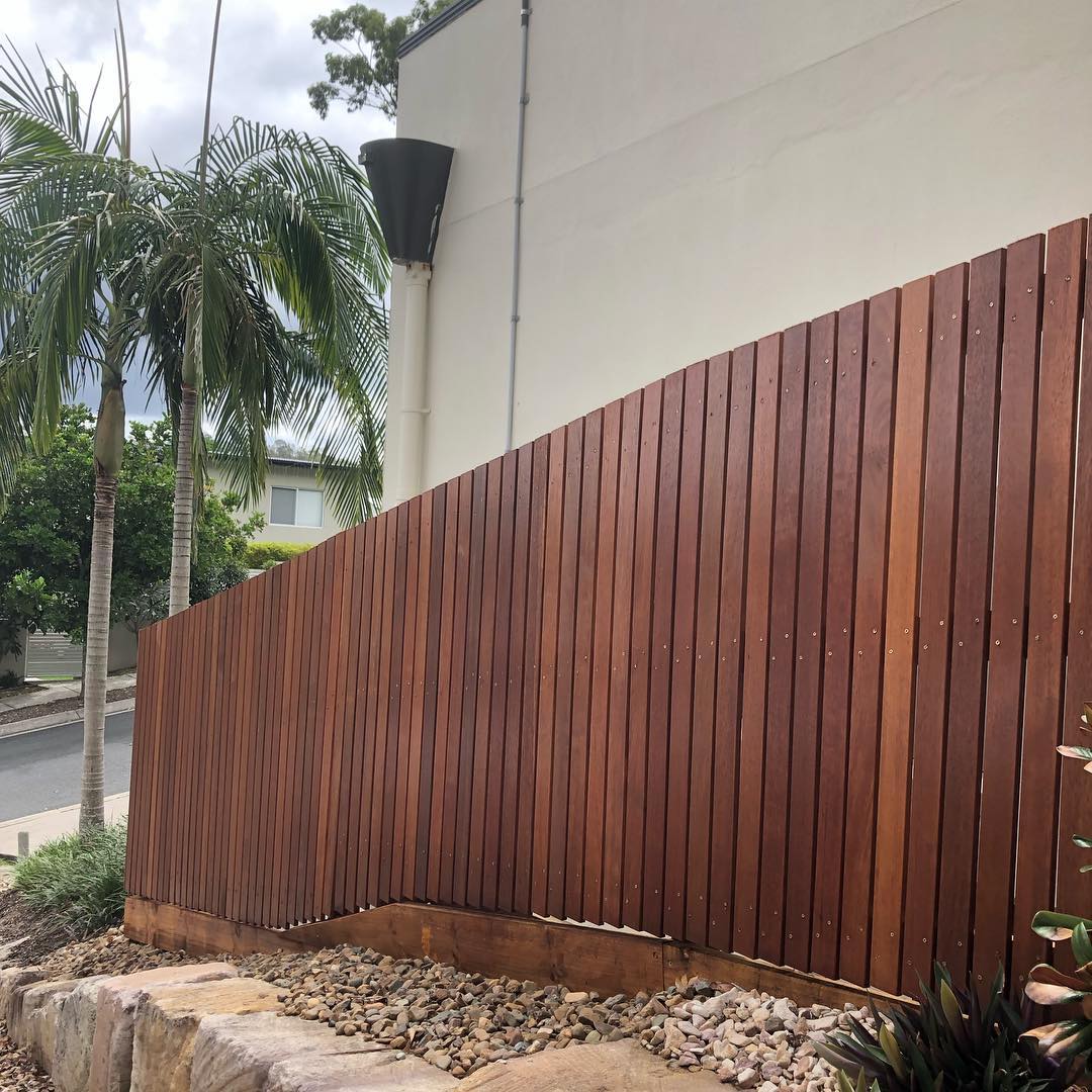 Oiled vertical timber batten fence beside a rendered building