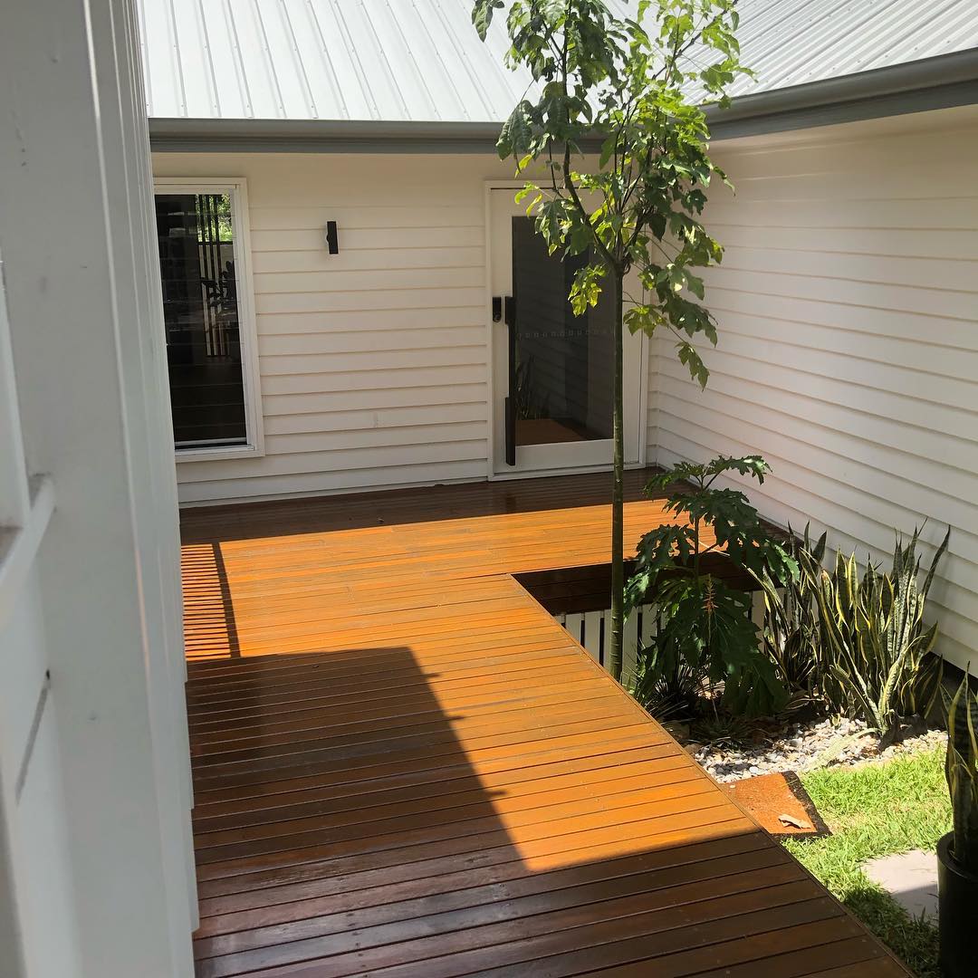 Freshly oiled timber walkway deck beside a white weatherboard house