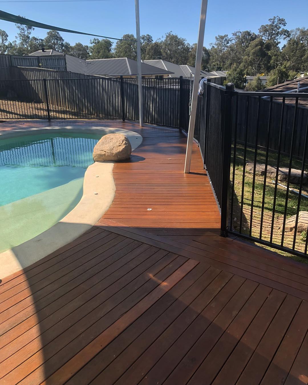 Oiled timber deck beside a freeform pool with black pool fencing