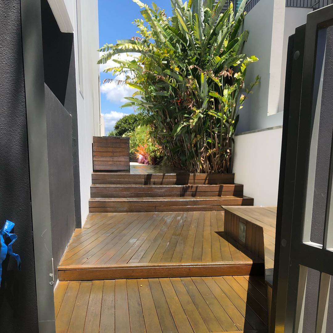 Oiled timber deck and steps between dark walls up to a garden