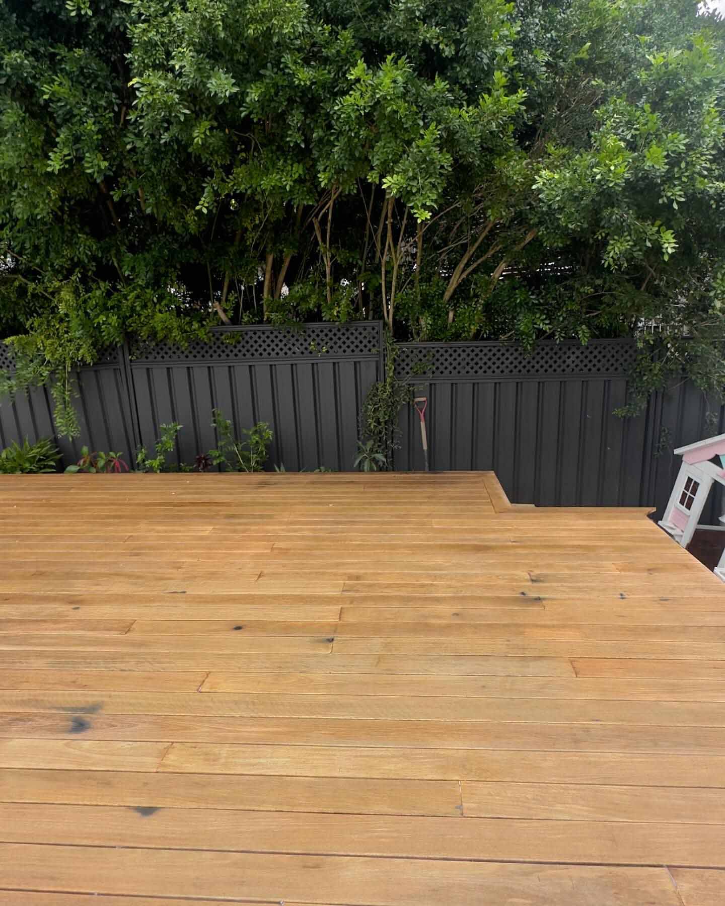 Freshly sanded bare timber deck in front of a grey fence and hedge