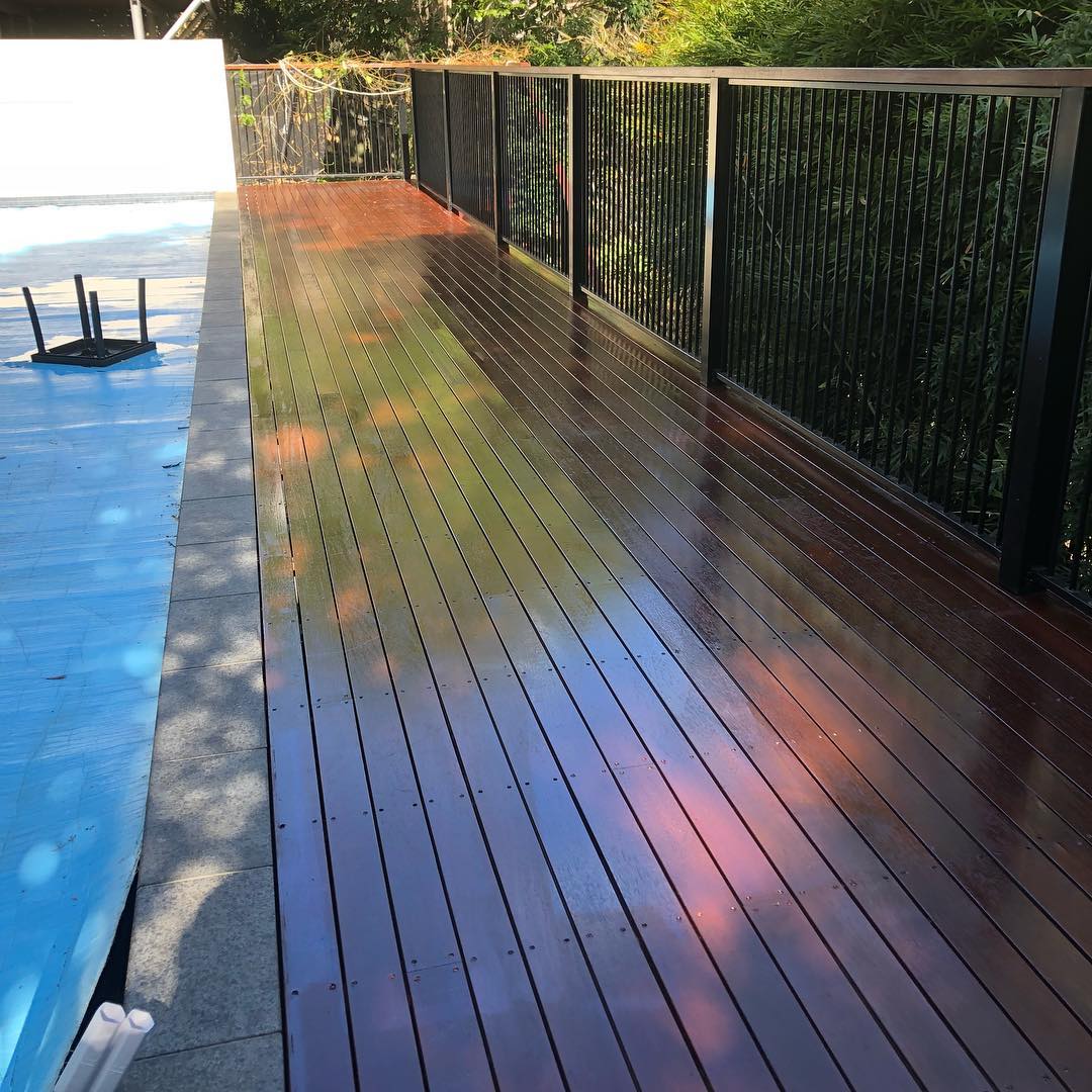 Glossy oiled timber deck between a covered pool and black pool fencing