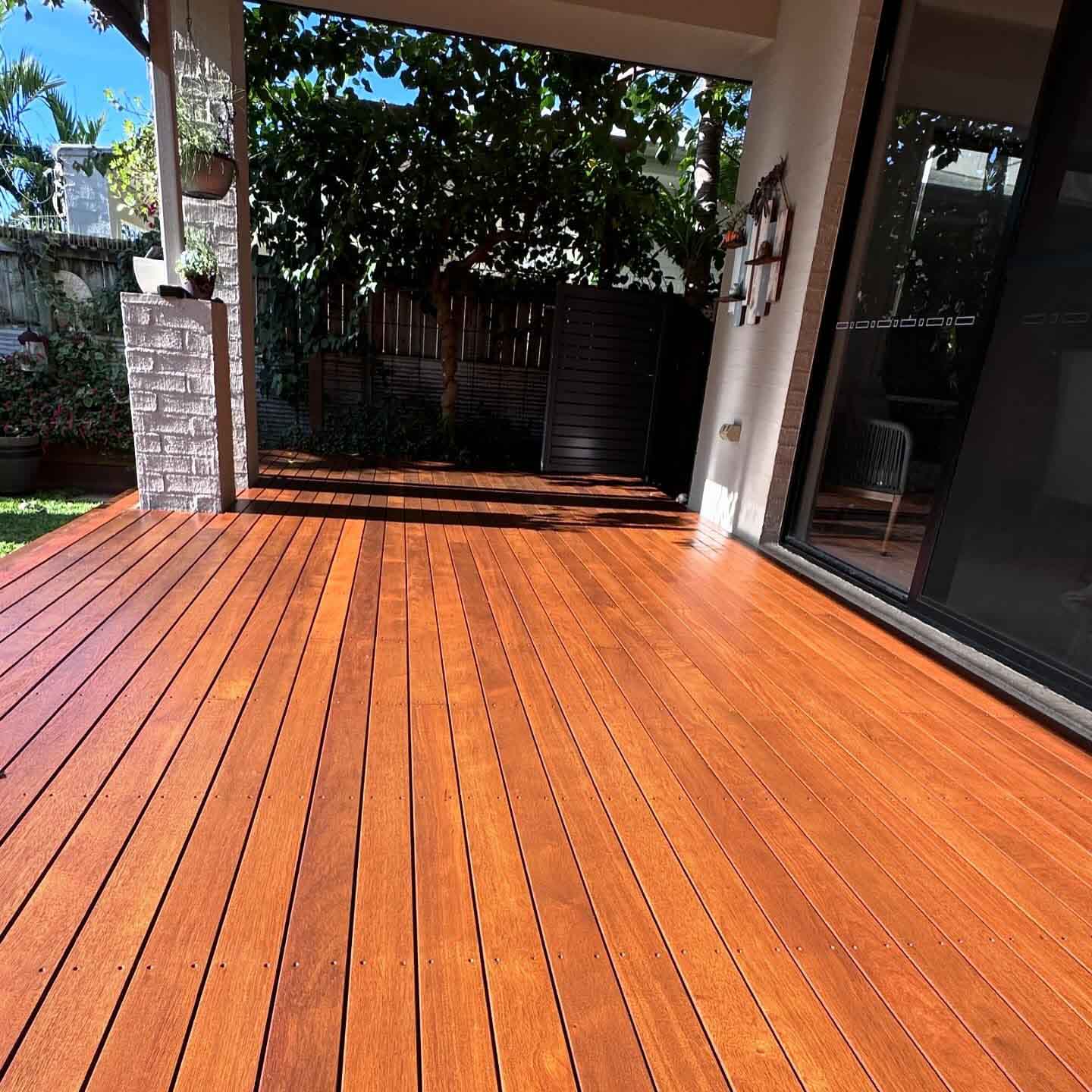 Orange-toned oiled timber deck under a patio, looking out to the garden