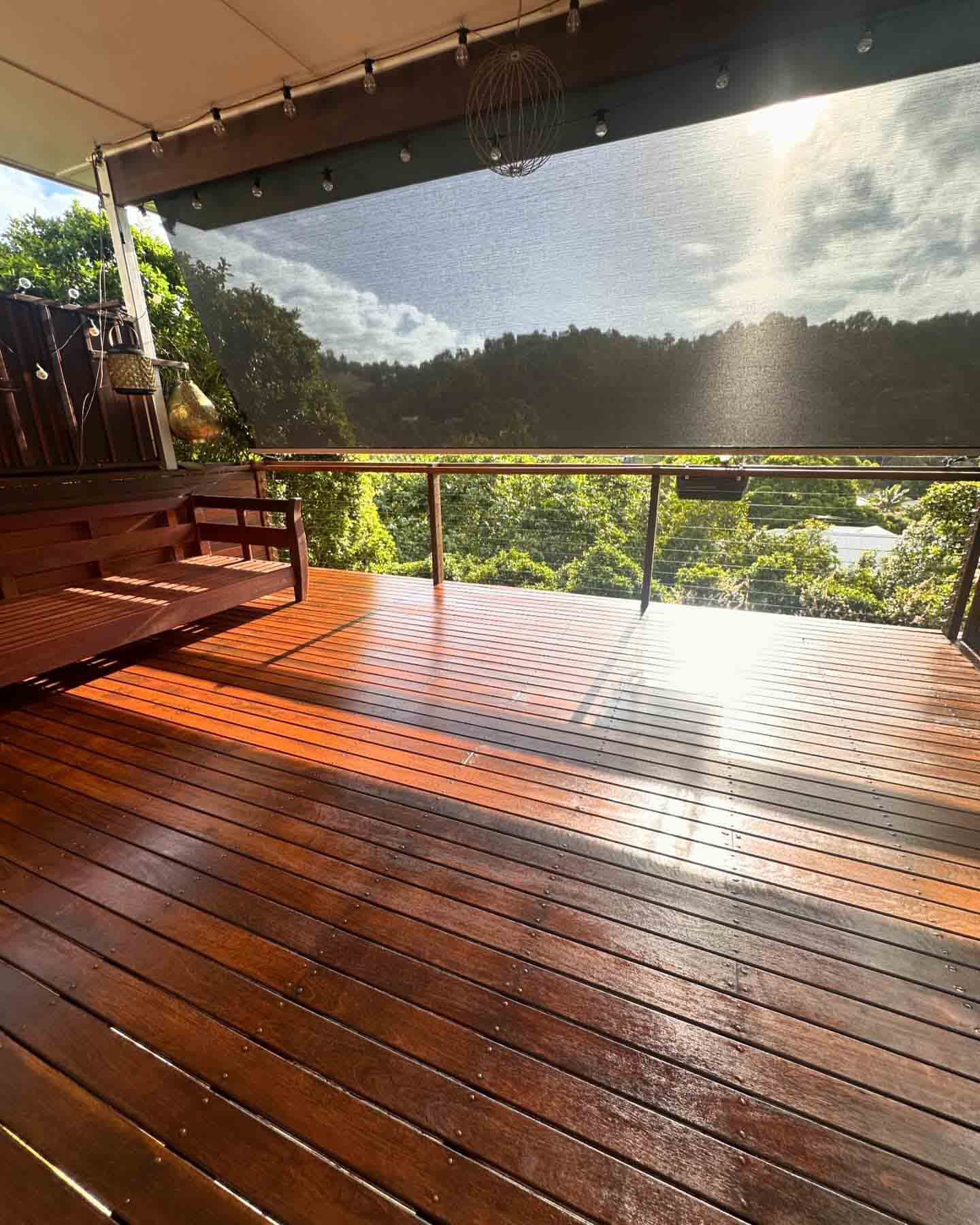 Glossy oiled timber deck with glass balustrade overlooking a green valley