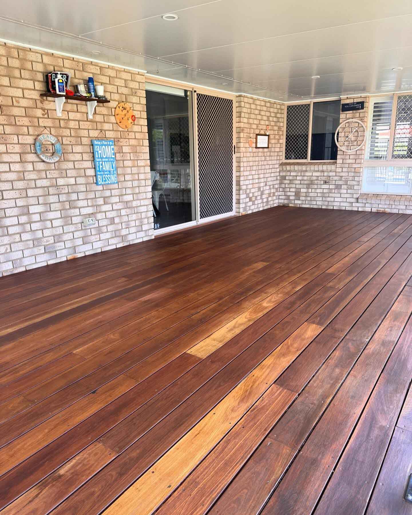 Oiled timber deck under a patio roof against a brick wall