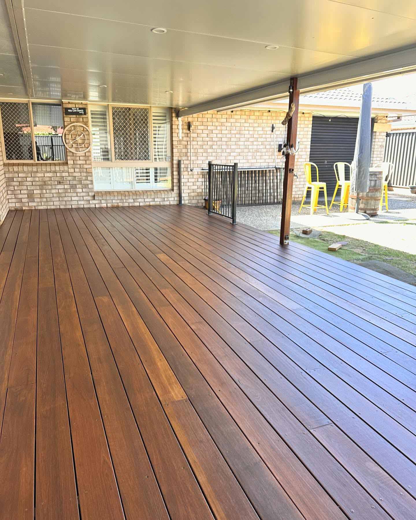 Oiled timber deck under a patio roof beside a brick house and side lawn