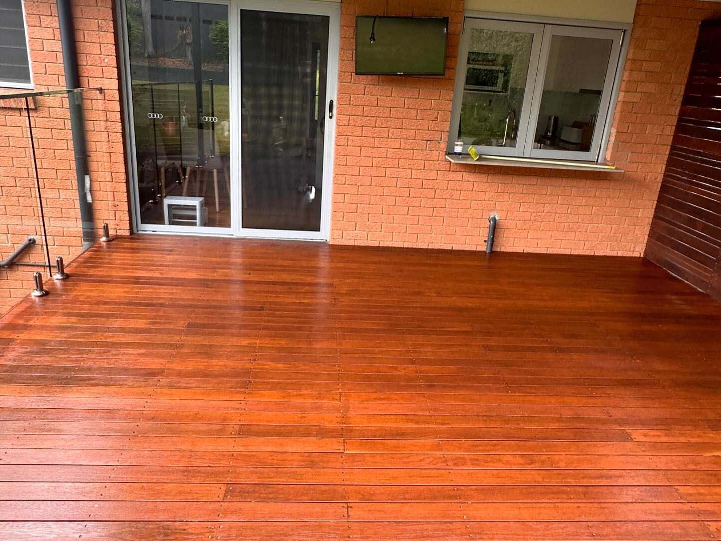 Glossy freshly oiled timber deck against an orange brick wall with a sliding door
