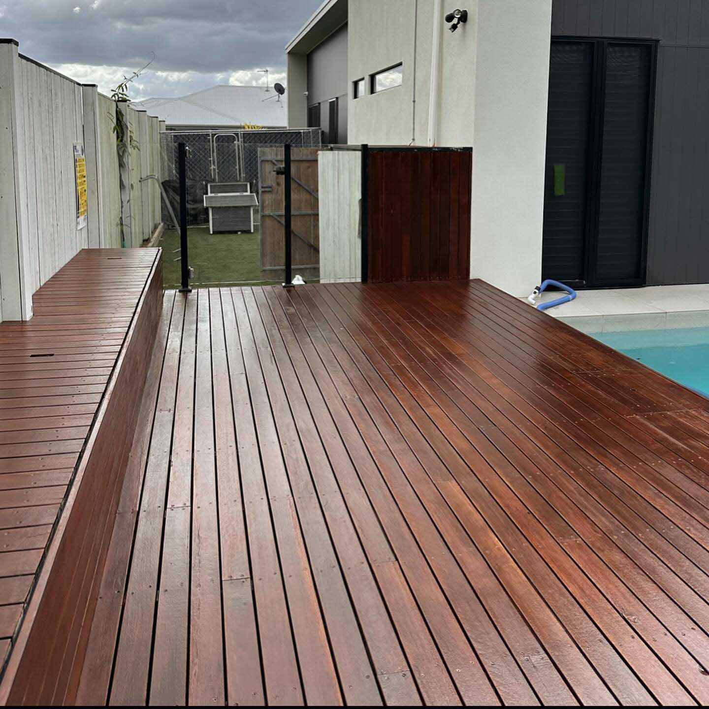 Dark oiled timber deck with a built-in timber bench beside a pool