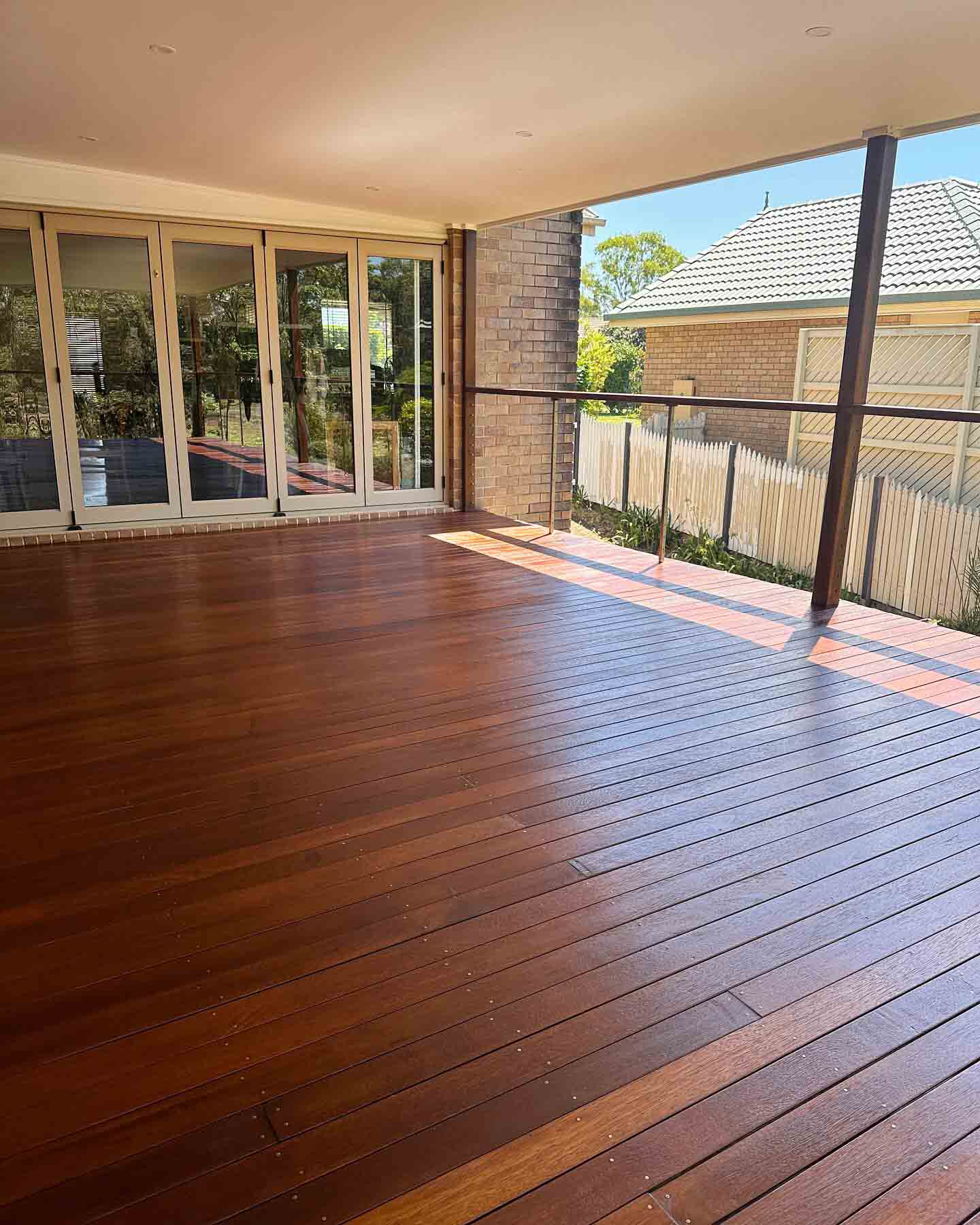 Covered oiled timber deck beside bi-fold doors and a brick pillar