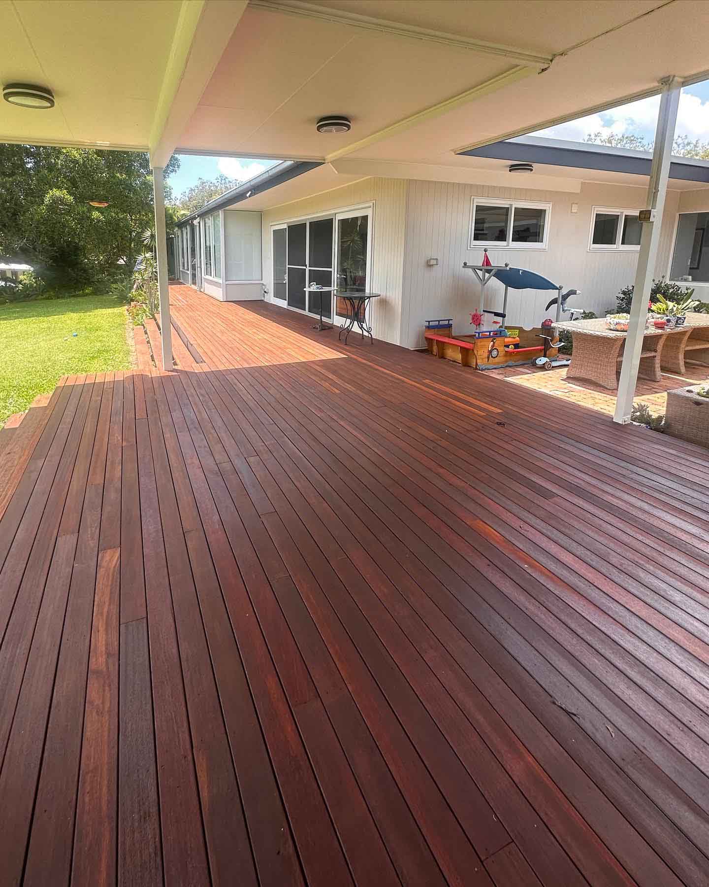Long covered timber deck running along a house towards a lawn