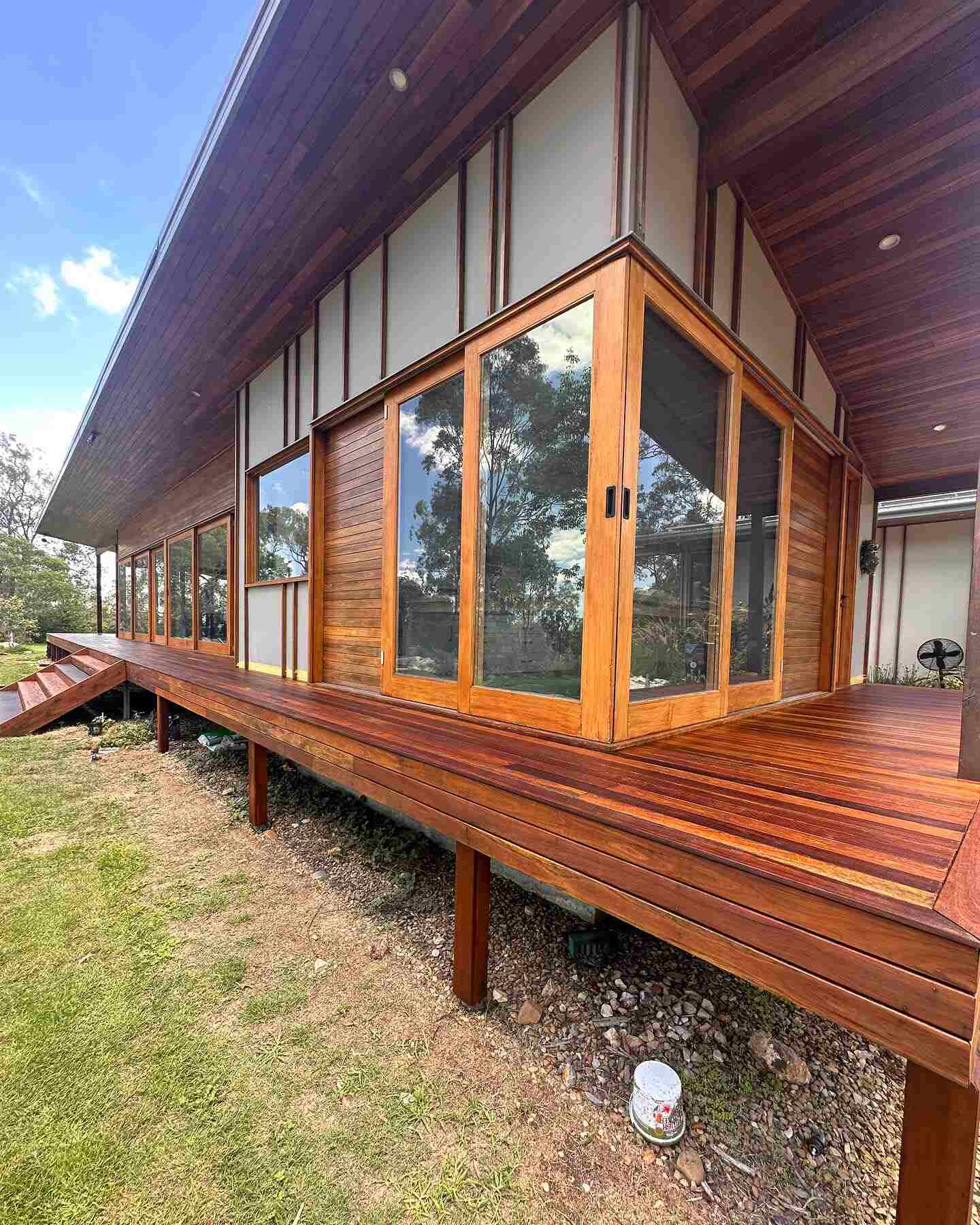 Raised timber deck on posts around a timber-clad house with tall windows