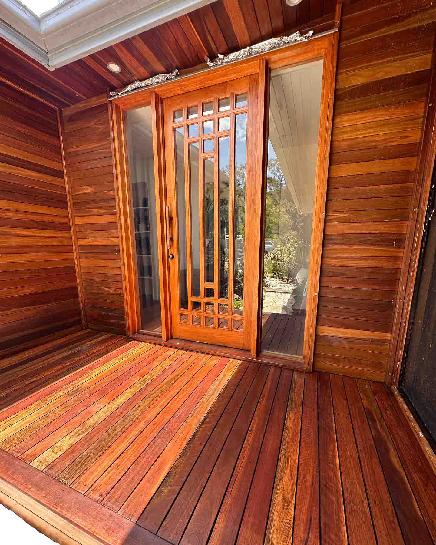 Oiled timber entry deck in front of a timber door and timber-clad walls