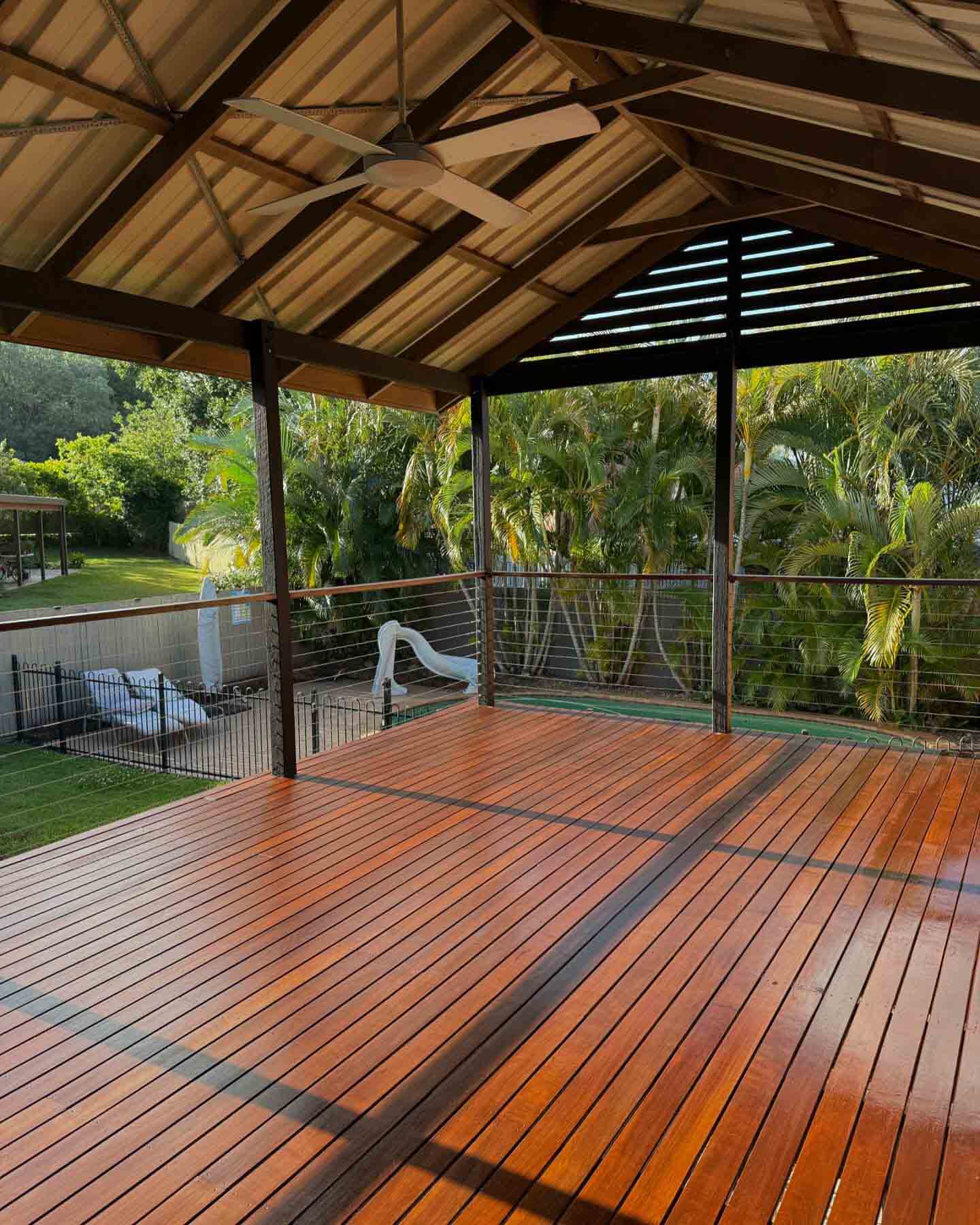 Oiled timber deck under a gabled timber-beamed roof overlooking a pool