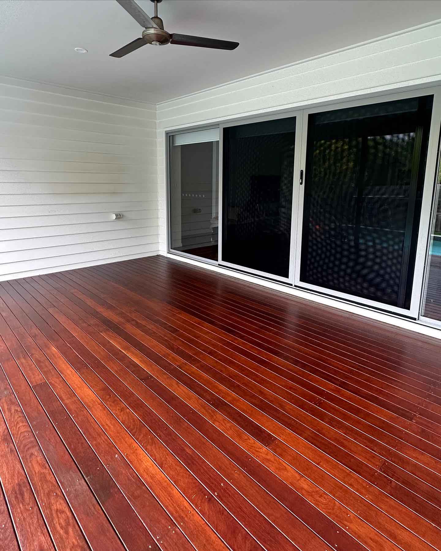 Glossy oiled timber deck outside black-framed sliding doors under a ceiling fan