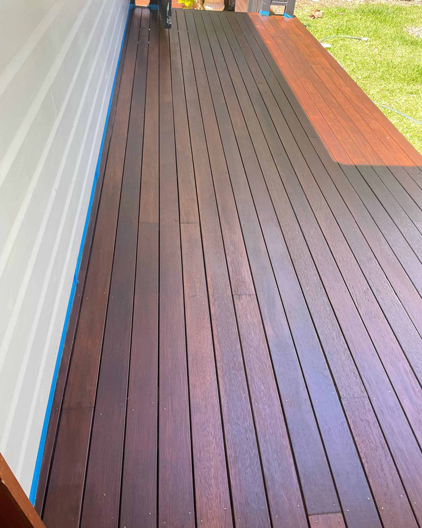 Narrow oiled timber deck along a weatherboard wall with blue masking tape at the edge