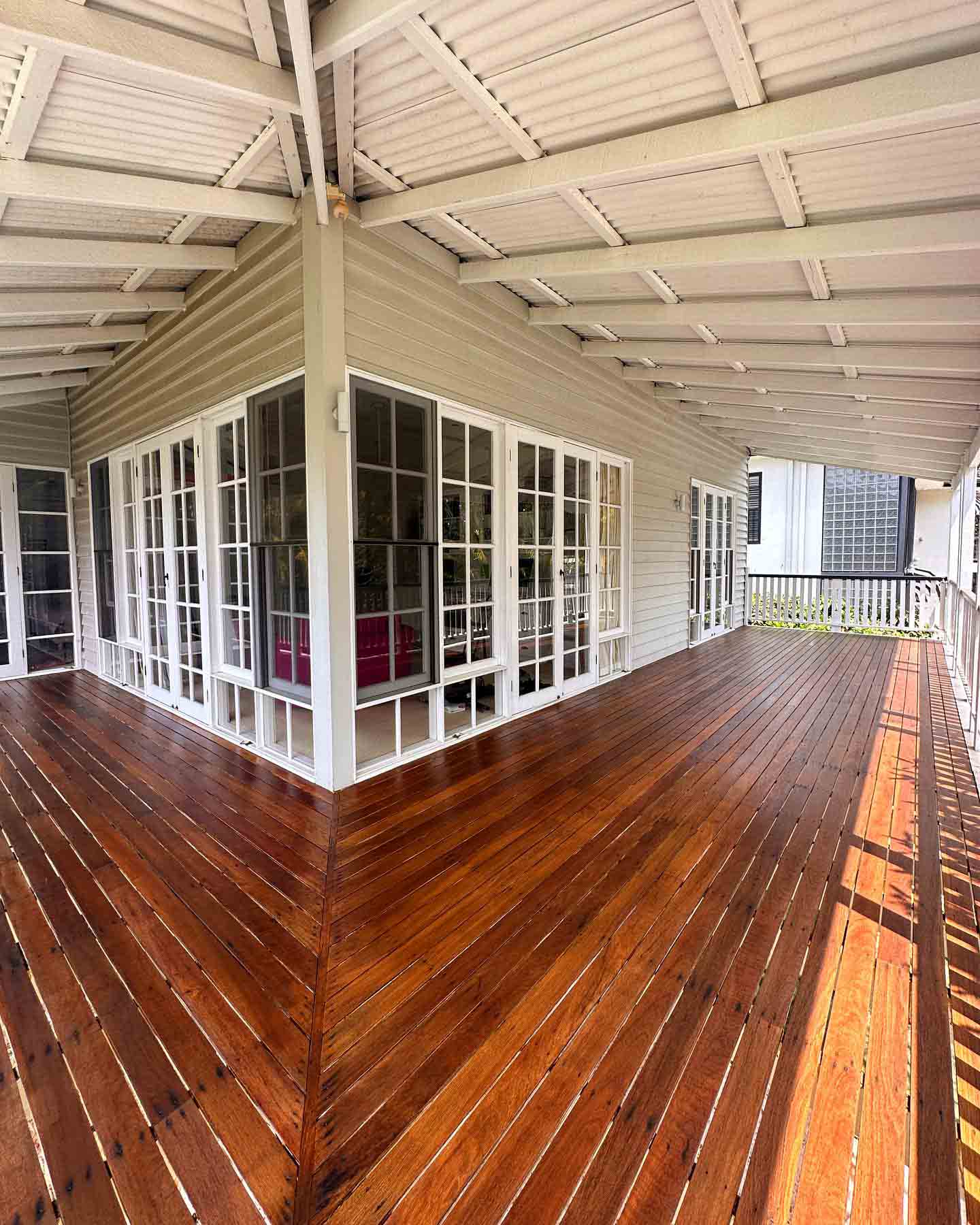 Wraparound oiled timber verandah beside white French doors under a white roof