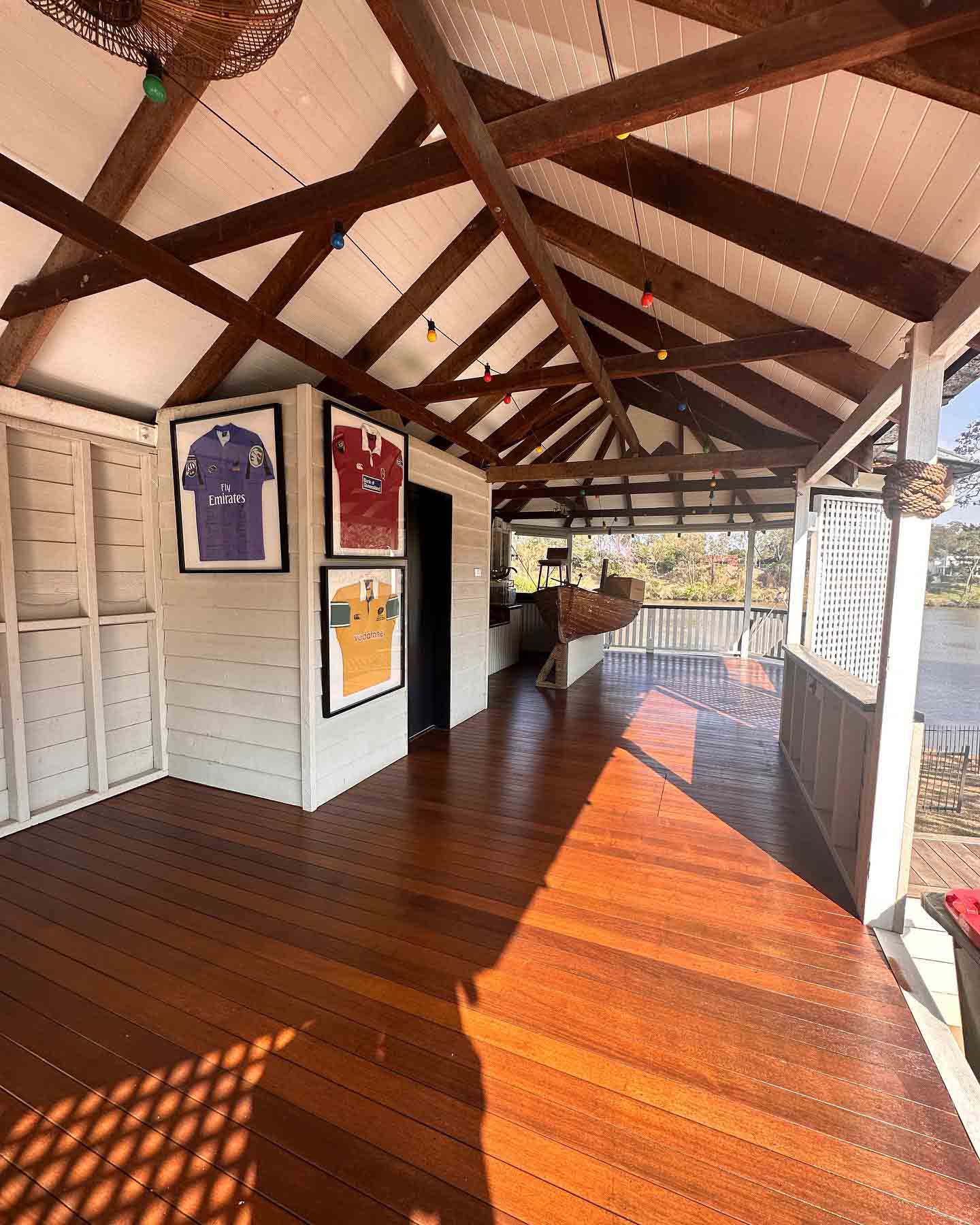 Oiled timber verandah under an exposed timber-truss roof with framed jerseys on the wall