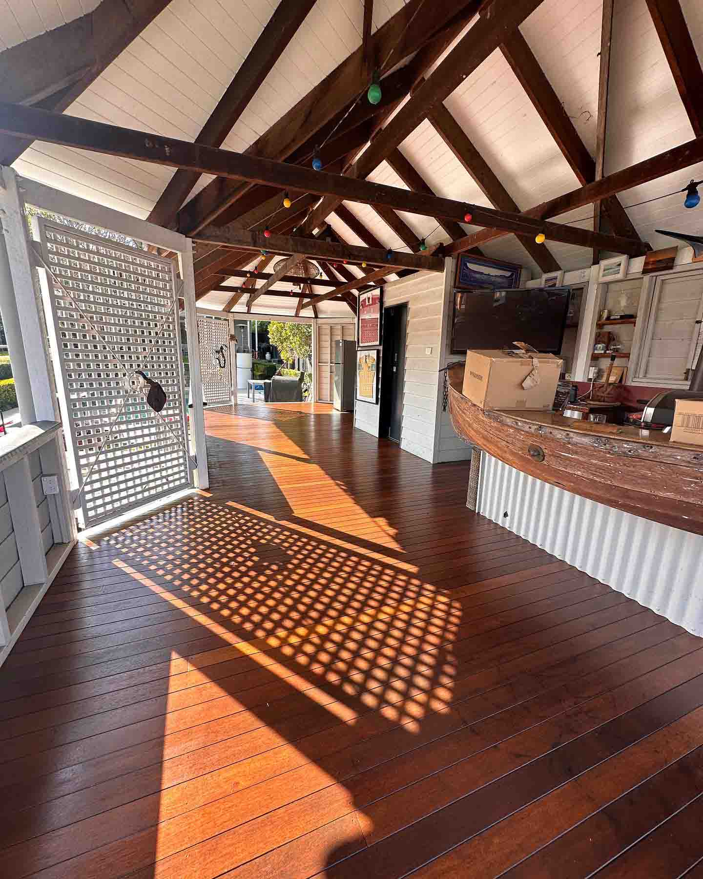 Oiled timber deck under a timber-truss roof beside a curved outdoor bar