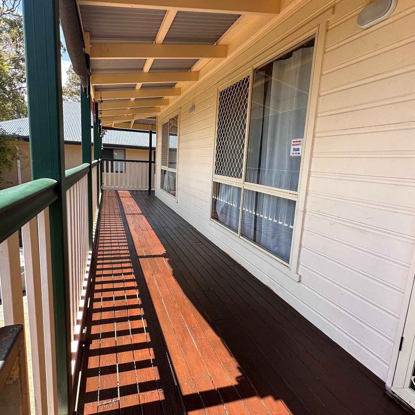 Narrow oiled timber verandah with green and white balustrade casting shadows