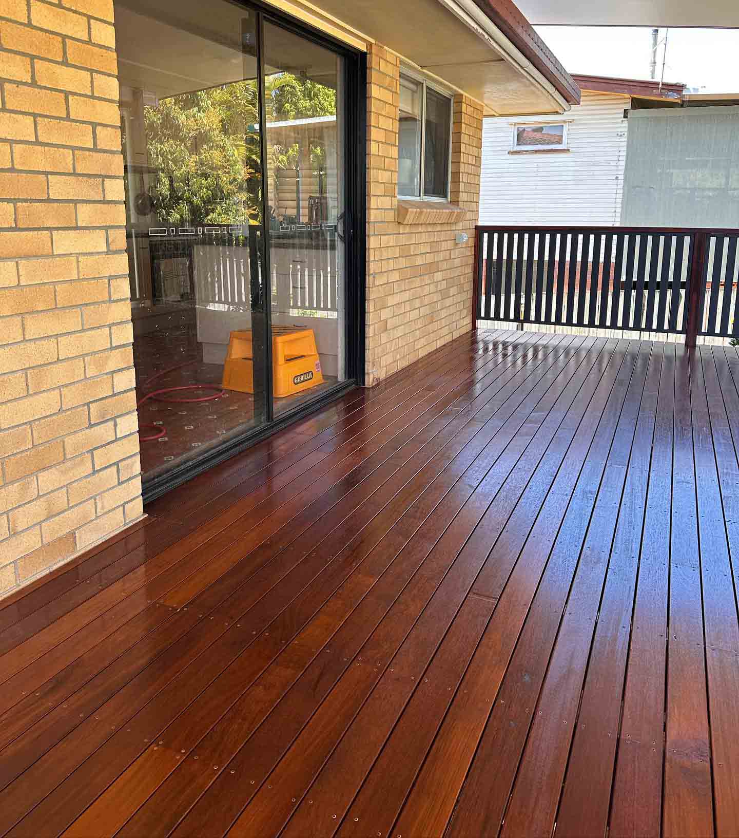 Glossy oiled timber deck beside a yellow brick wall with dark timber balustrade
